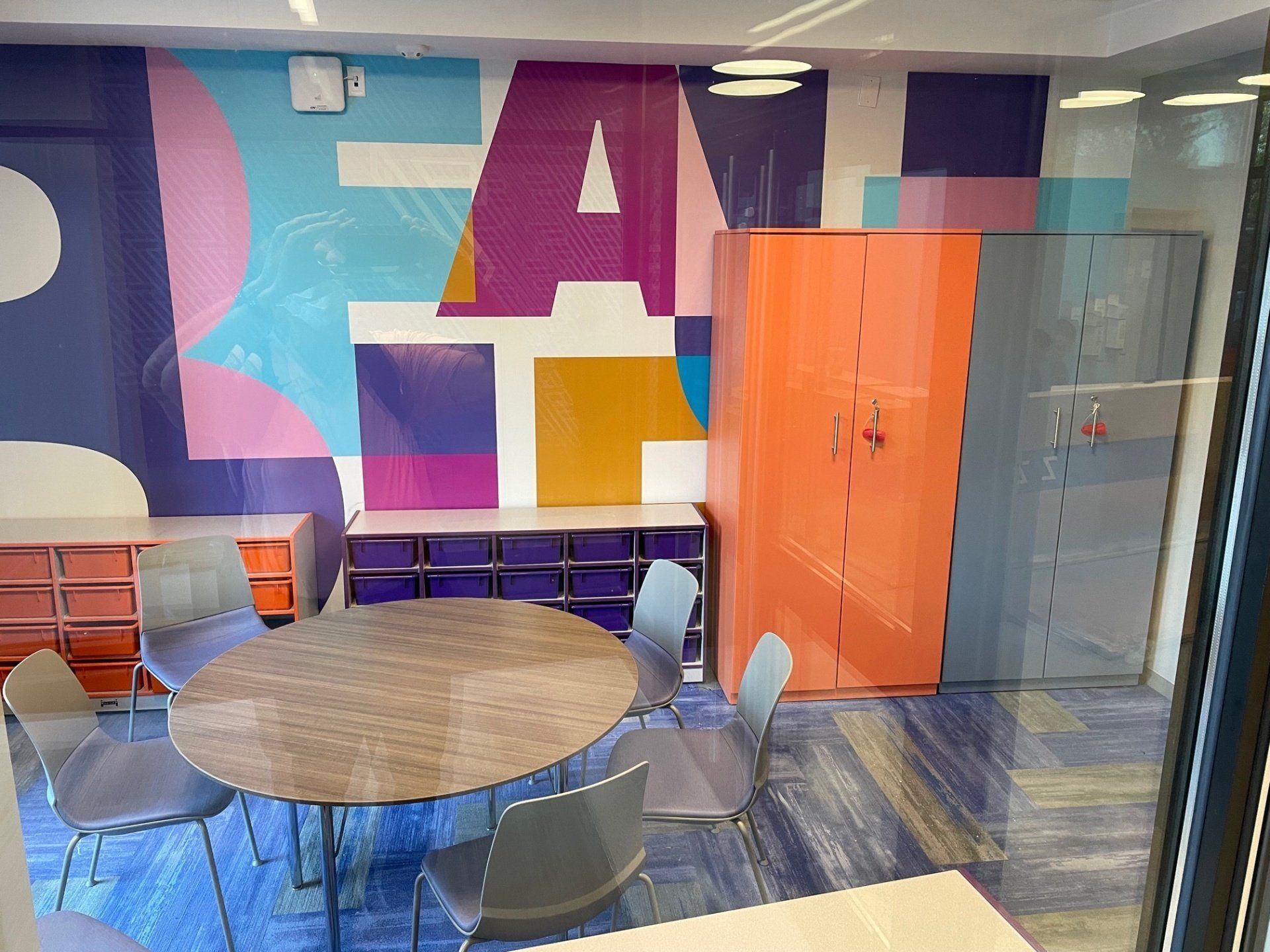 A room with a round table and chairs and a mural on the wall.