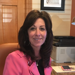 A woman in a pink jacket is smiling in front of a printer