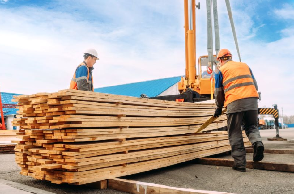 Workers loading stacked lumber onto a truck at a construction site