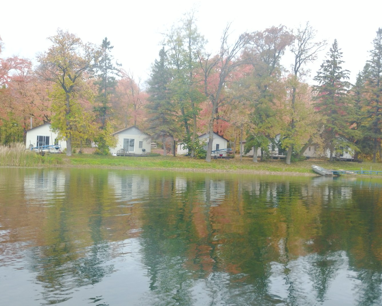 A lake with houses on the shore and trees reflected in the water.