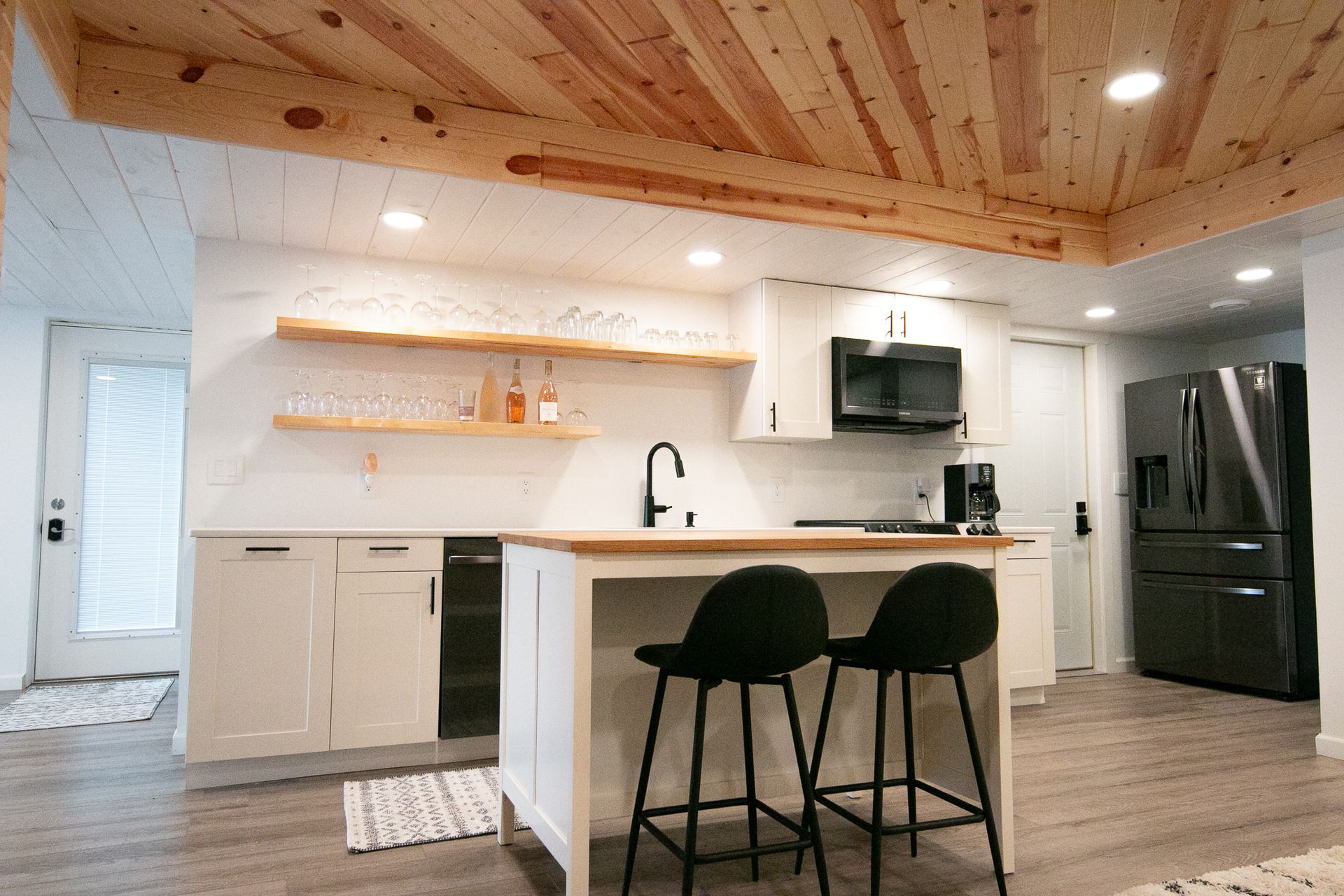 A kitchen with white cabinets , black appliances , and a wooden ceiling.