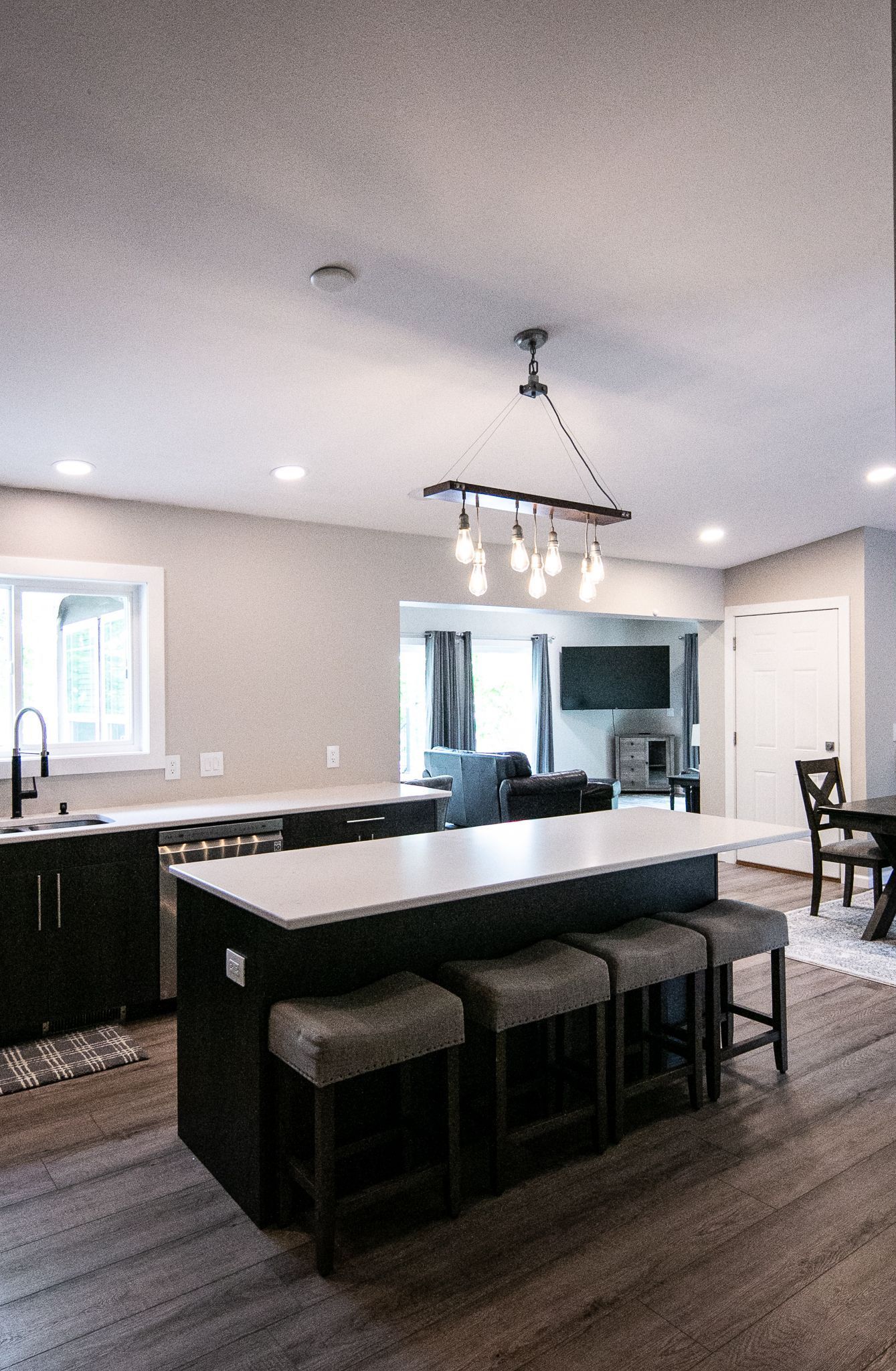 A kitchen with a large island and stools and a chandelier hanging from the ceiling.