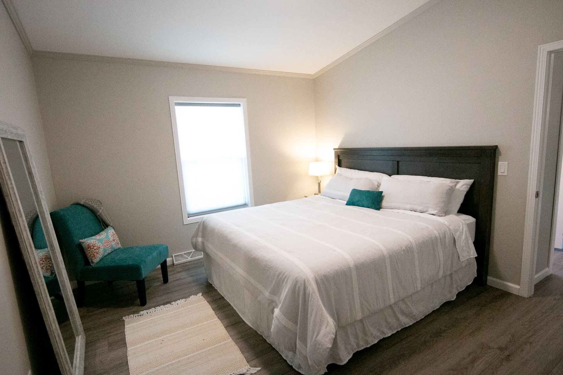 A bedroom with a king size bed , chair , mirror and window.