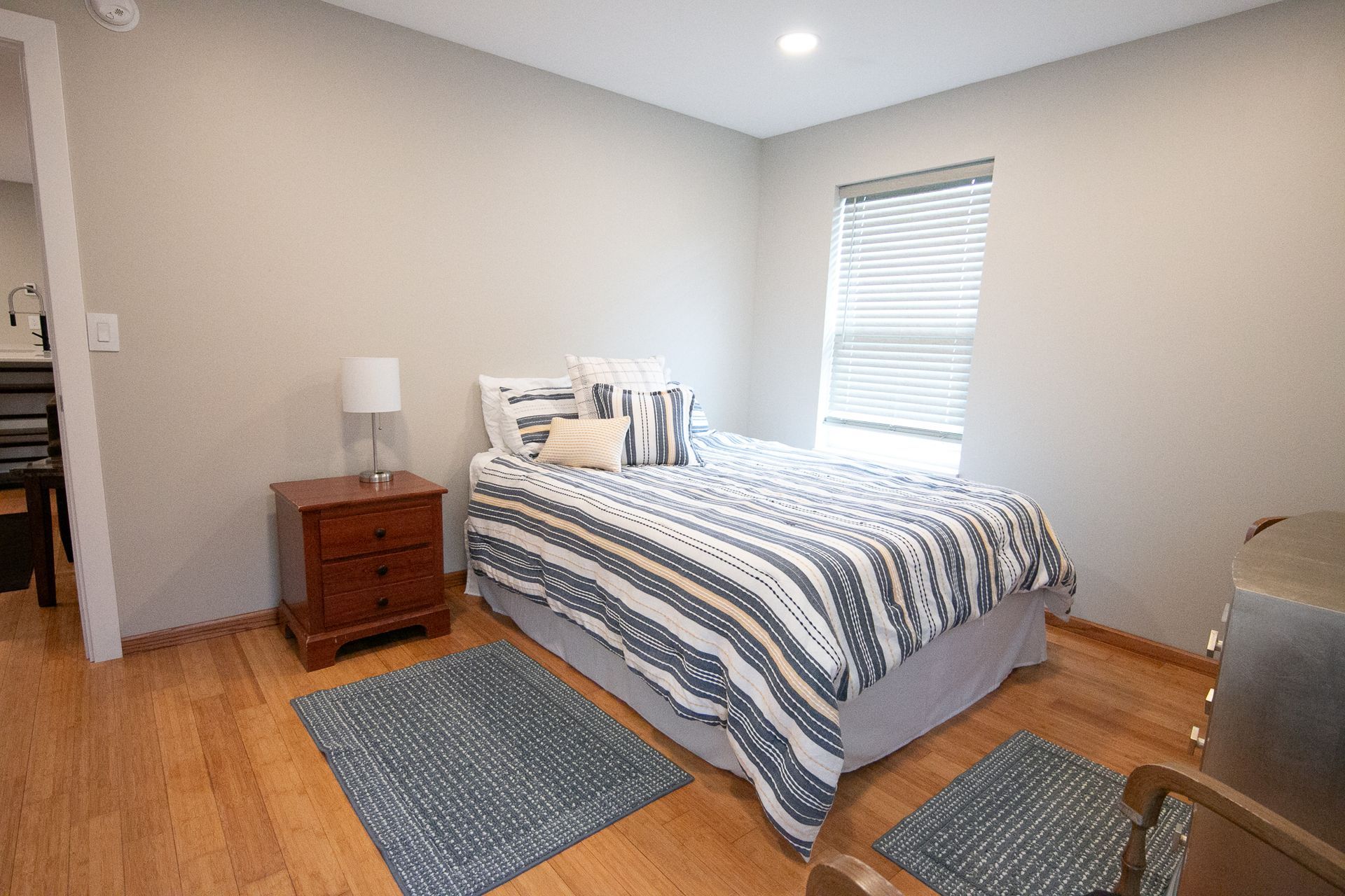 A bedroom with a bed , nightstand , rug and window.