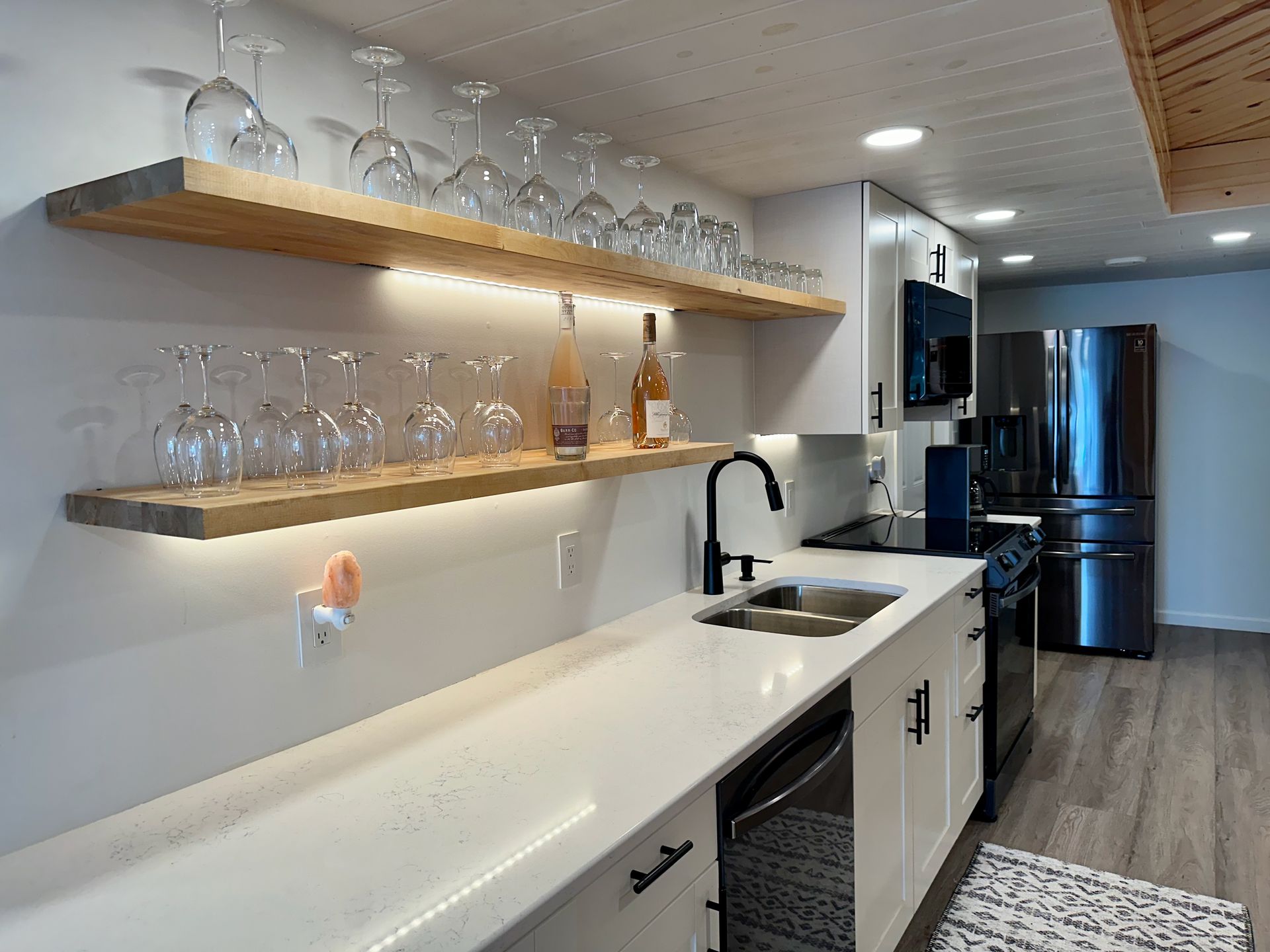 A kitchen with white cabinets , a sink , a refrigerator , and a shelf filled with wine glasses.