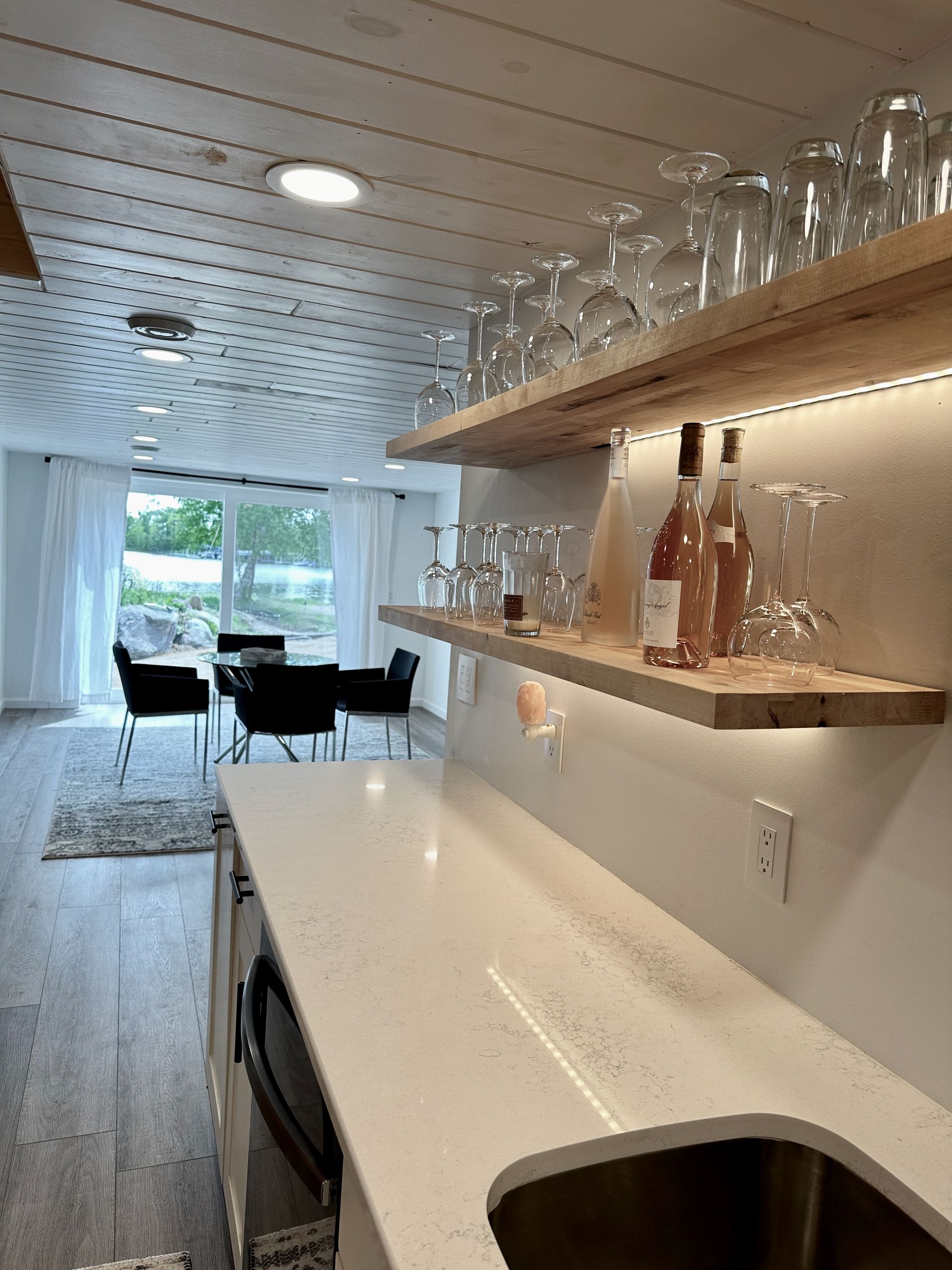A kitchen with a sink and a bottle of wine on a shelf.