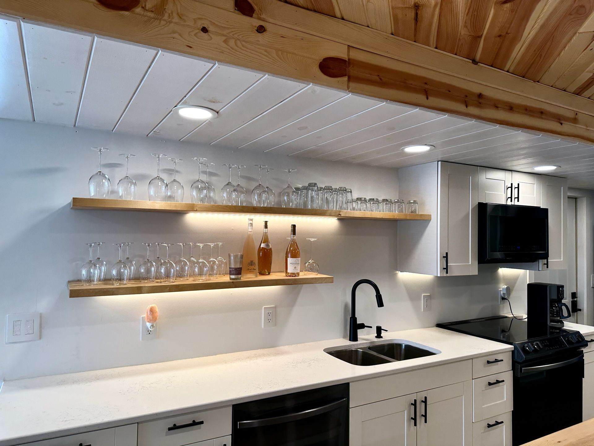 A kitchen with white cabinets , a sink , a stove and a bar.