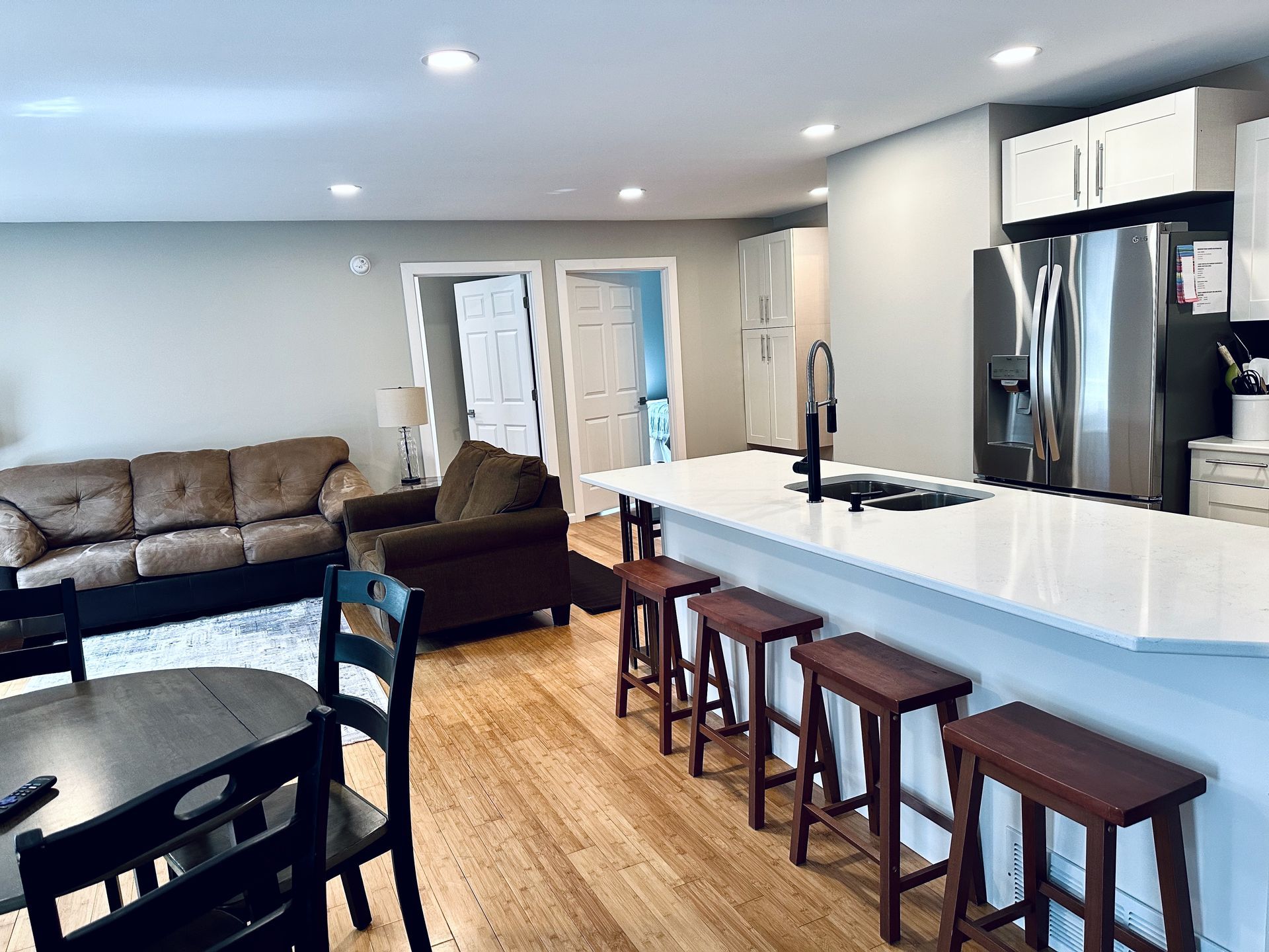 A living room with a couch , table , chairs and a kitchen with stools.