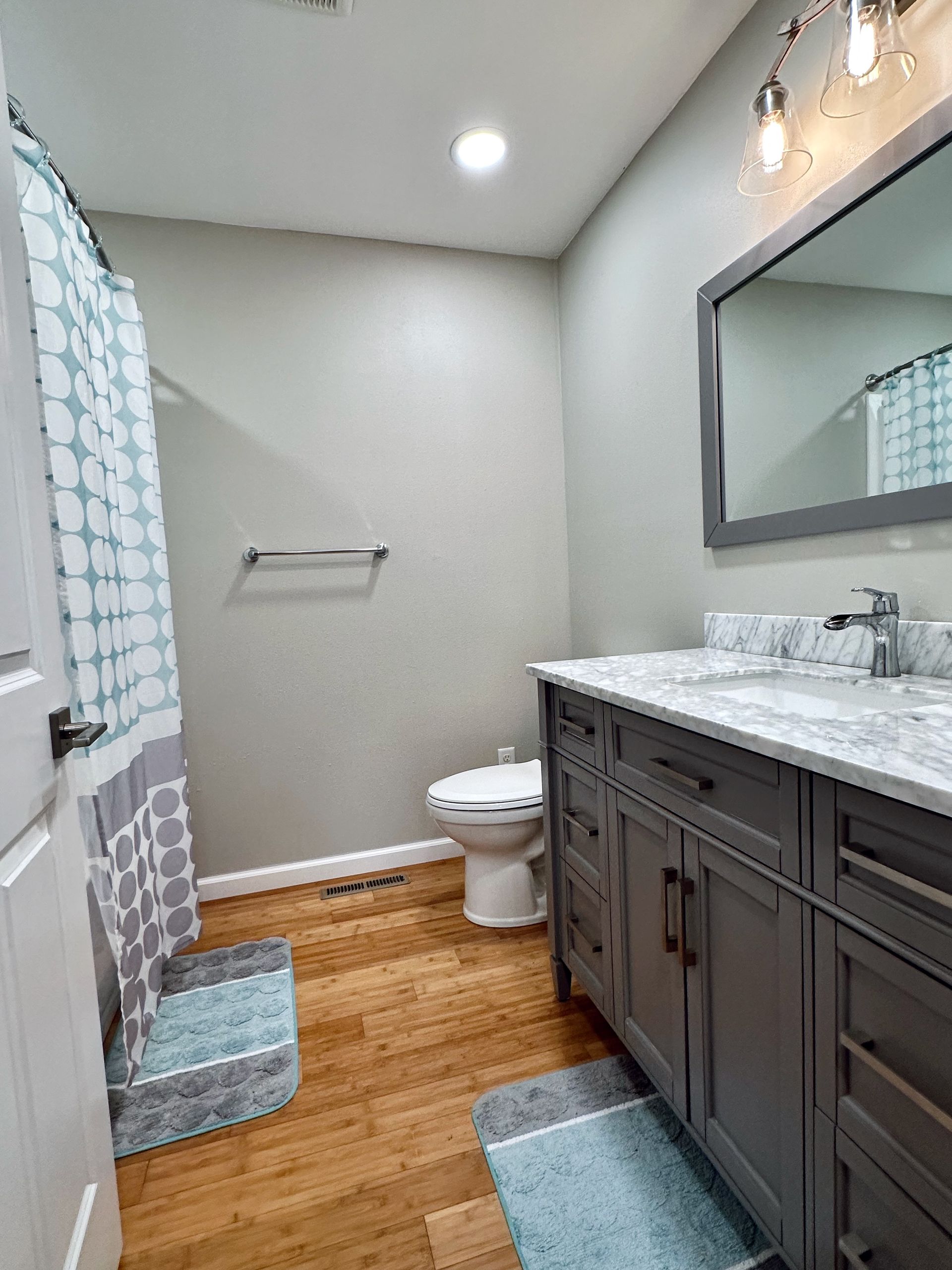 A bathroom with a toilet , sink , mirror and shower curtain.