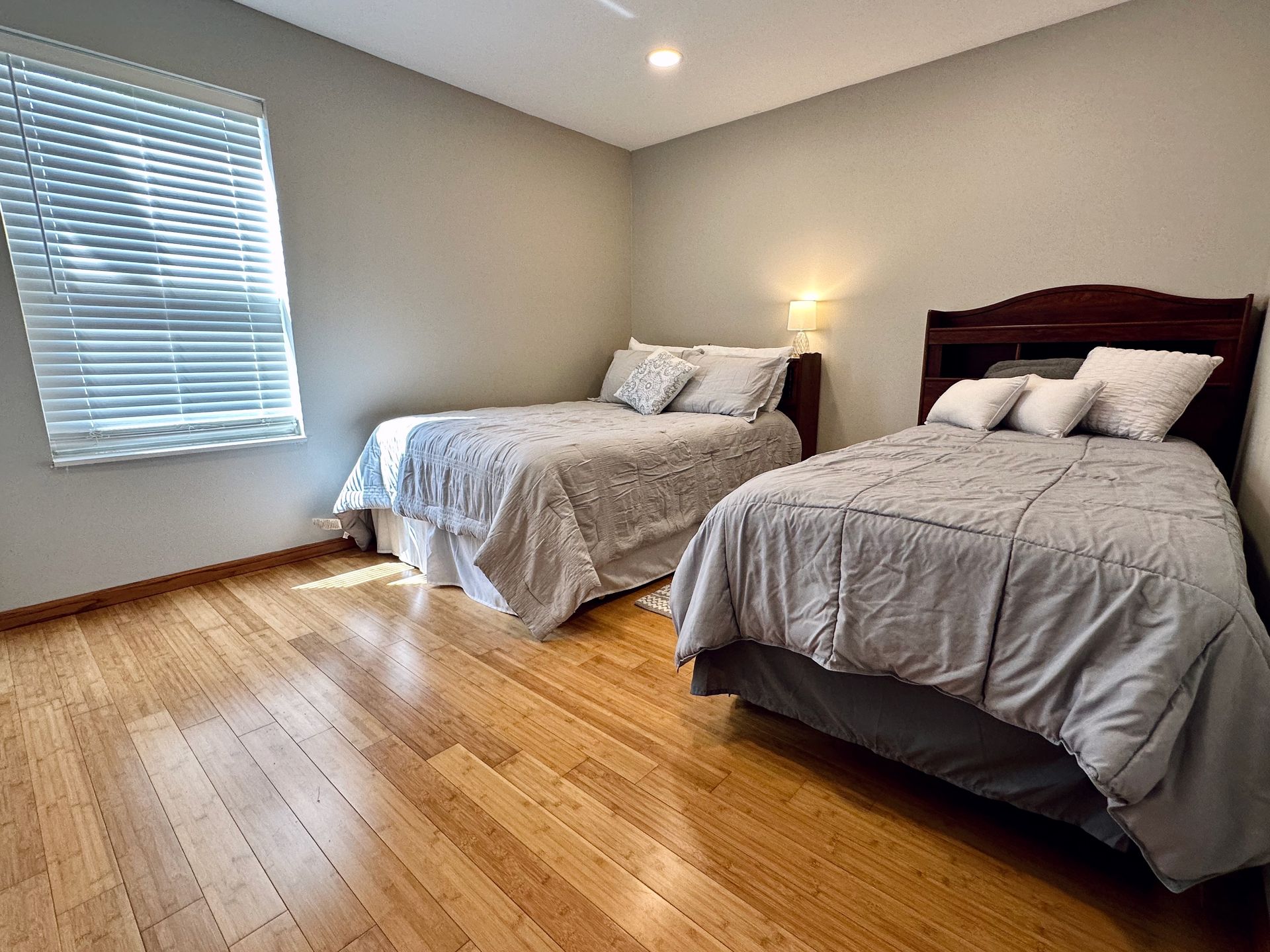 A bedroom with two beds and a window with blinds.