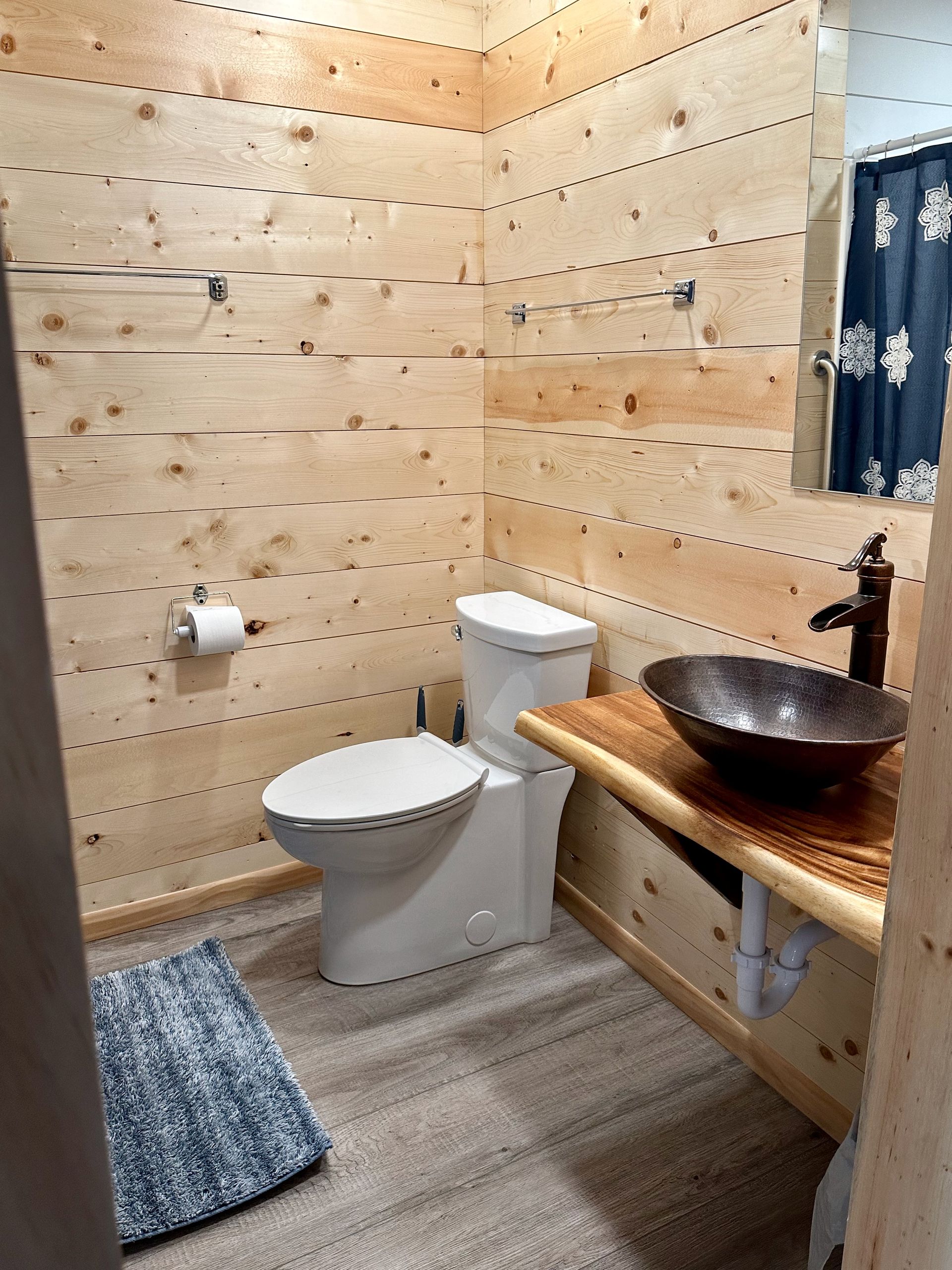 A bathroom with a toilet , sink , mirror and wooden walls.