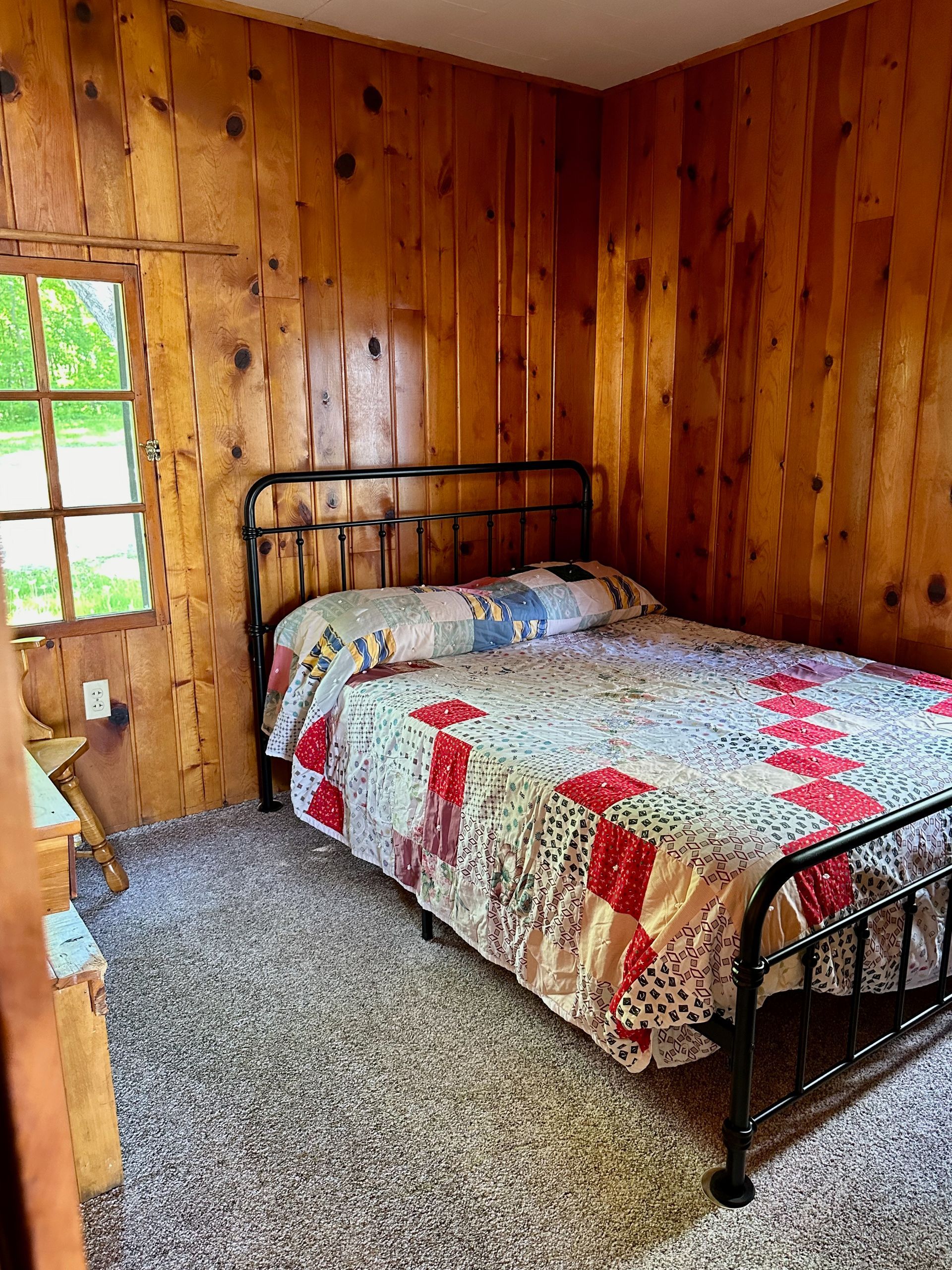 A bedroom with wood paneling and a bed with a quilt on it.