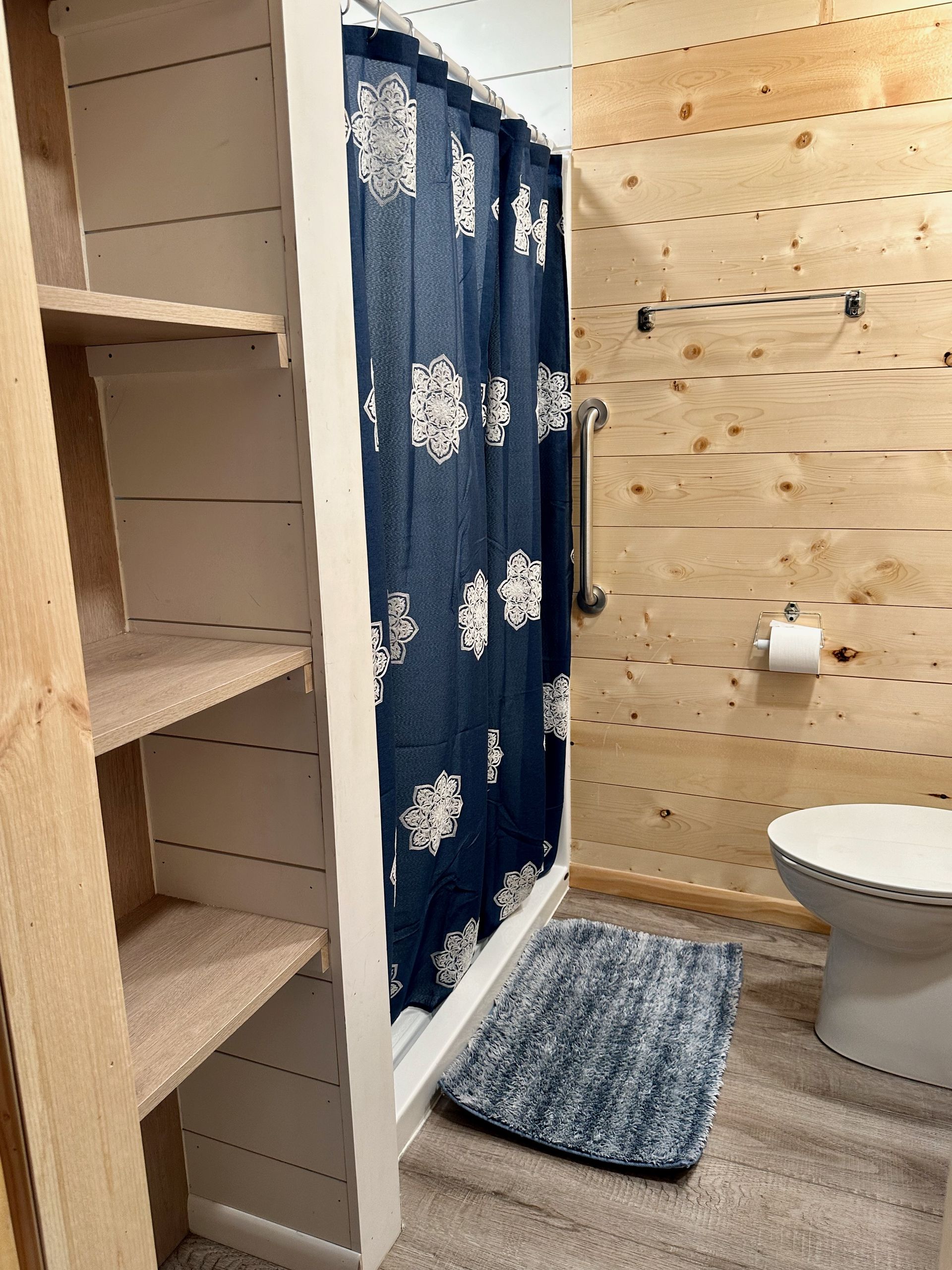A bathroom with a toilet , shower , and shelves.