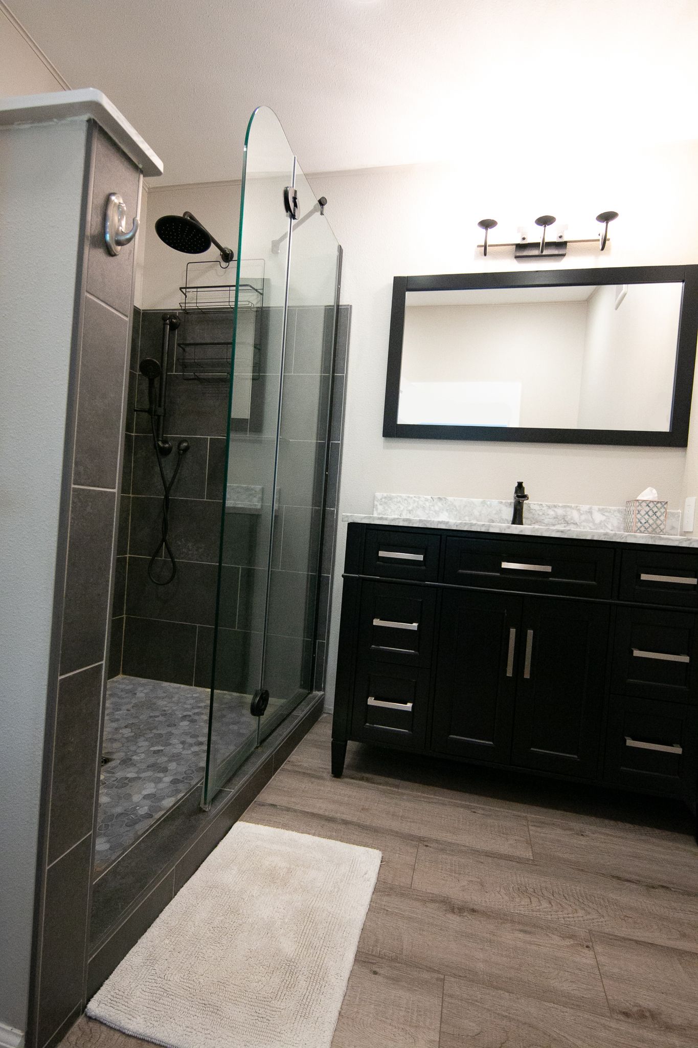A bathroom with a walk in shower , sink , mirror and vanity.