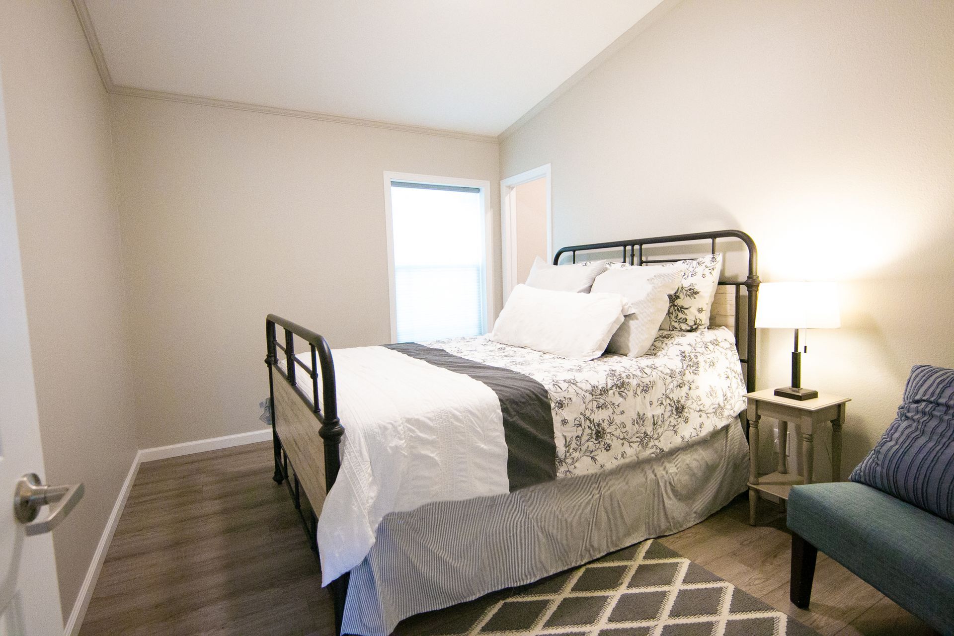 A bedroom with a bed , chair , lamp and window.