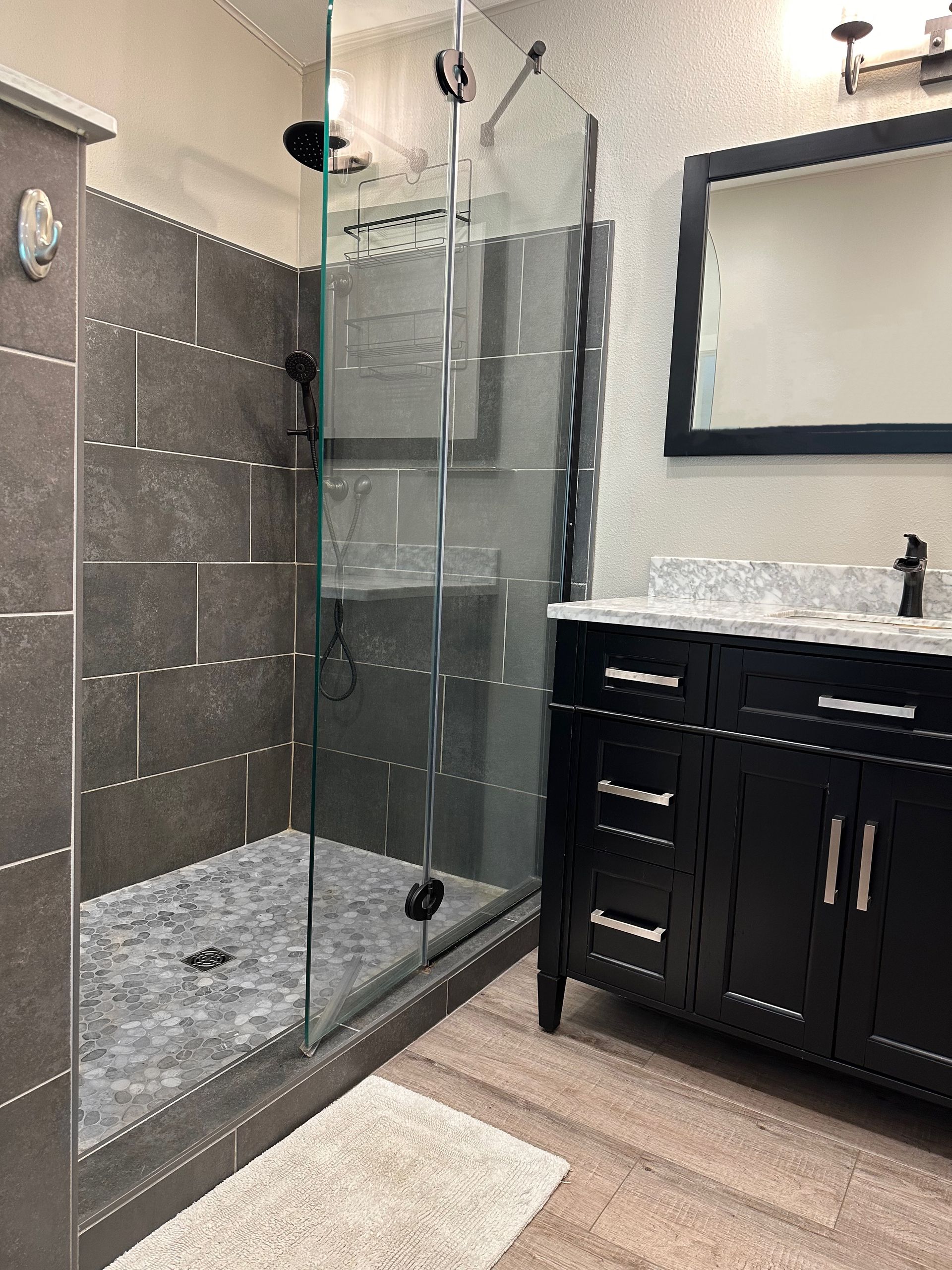 A bathroom with a walk in shower , sink , mirror and vanity.