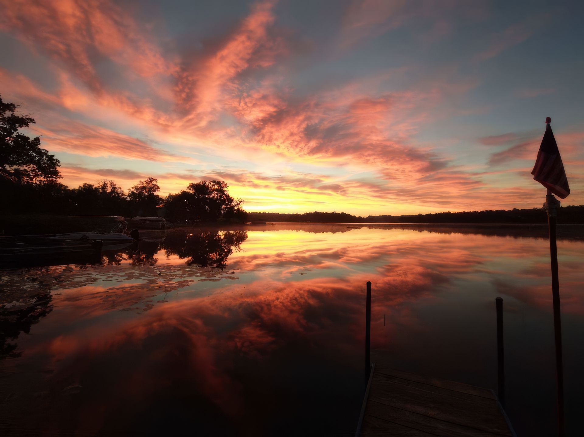 A sunset over a lake with a flag in the foreground