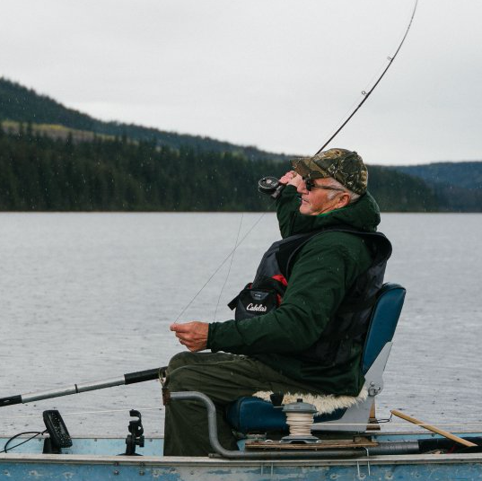 A man in a green jacket is fishing in a boat