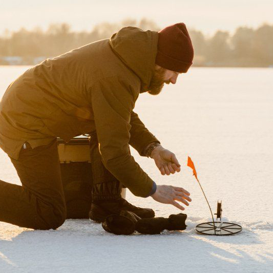 A man in a brown jacket is kneeling down in the snow