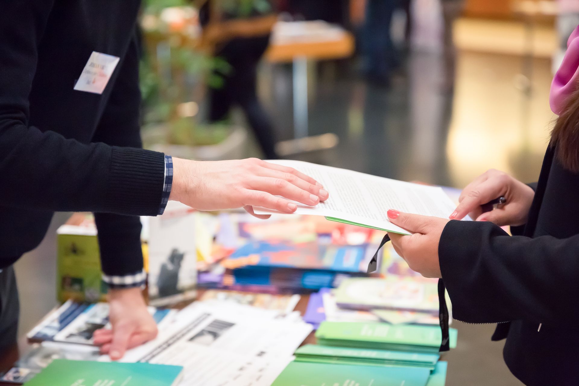 Person handing brochure to another person at a table with stacks of brochures.