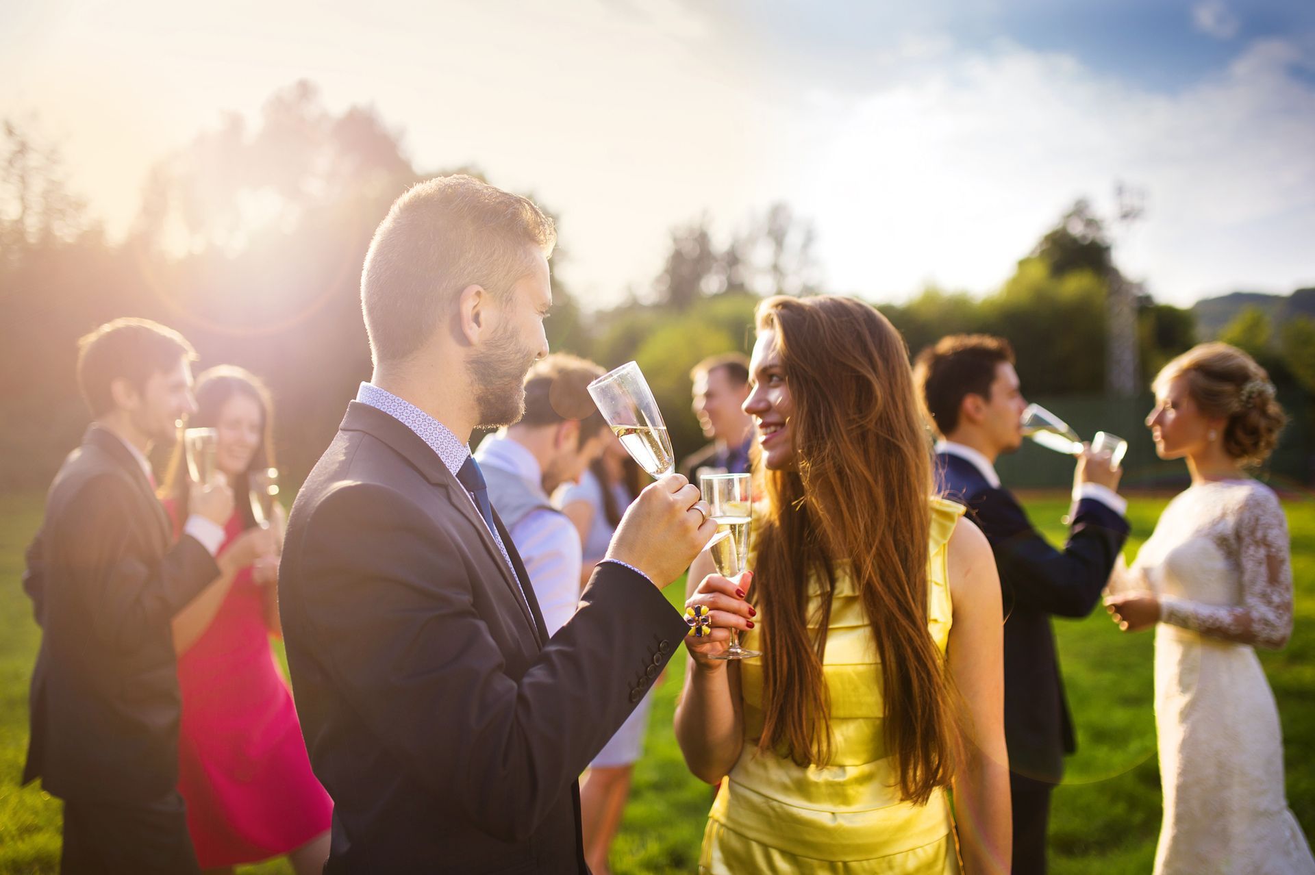 People toasting with champagne outdoors, sunny backdrop.