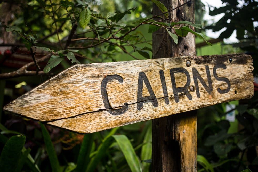 A Wooden Sign Pointing To Cairns Is Surrounded By Trees — Allpower Electrical Wholesalers Pty Ltd In Cairns, QLD