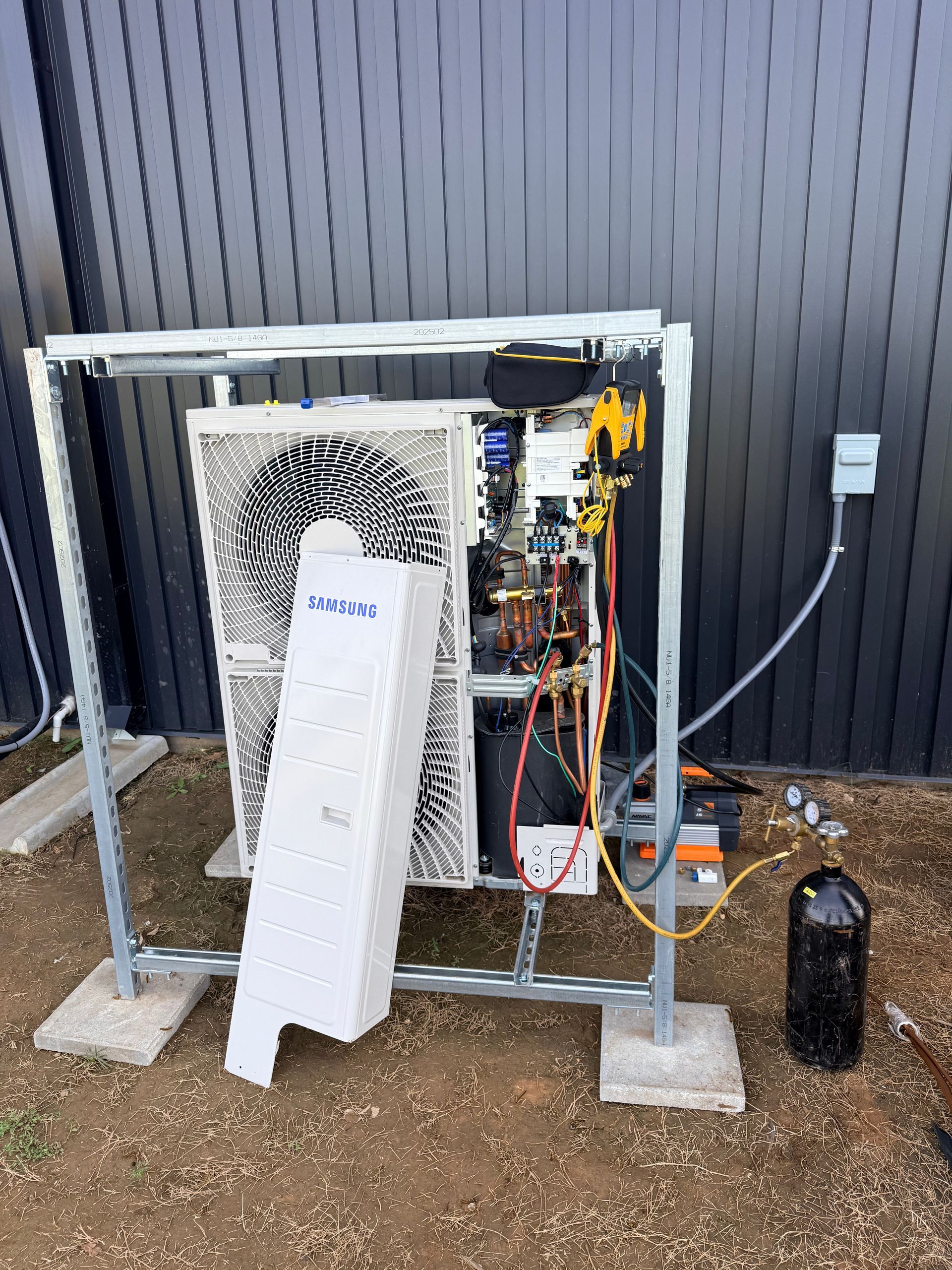Outdoor HVAC unit beside a gray building, with the metal frame and front panel open showing wiring.