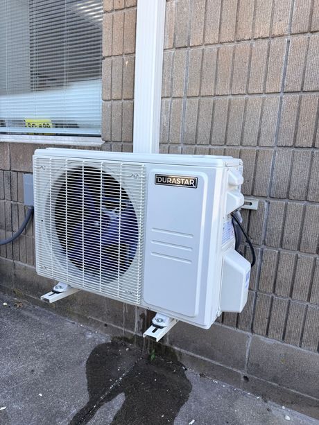 Outdoor wall-mounted air conditioner unit with a protective fan cover on a stone building wall.