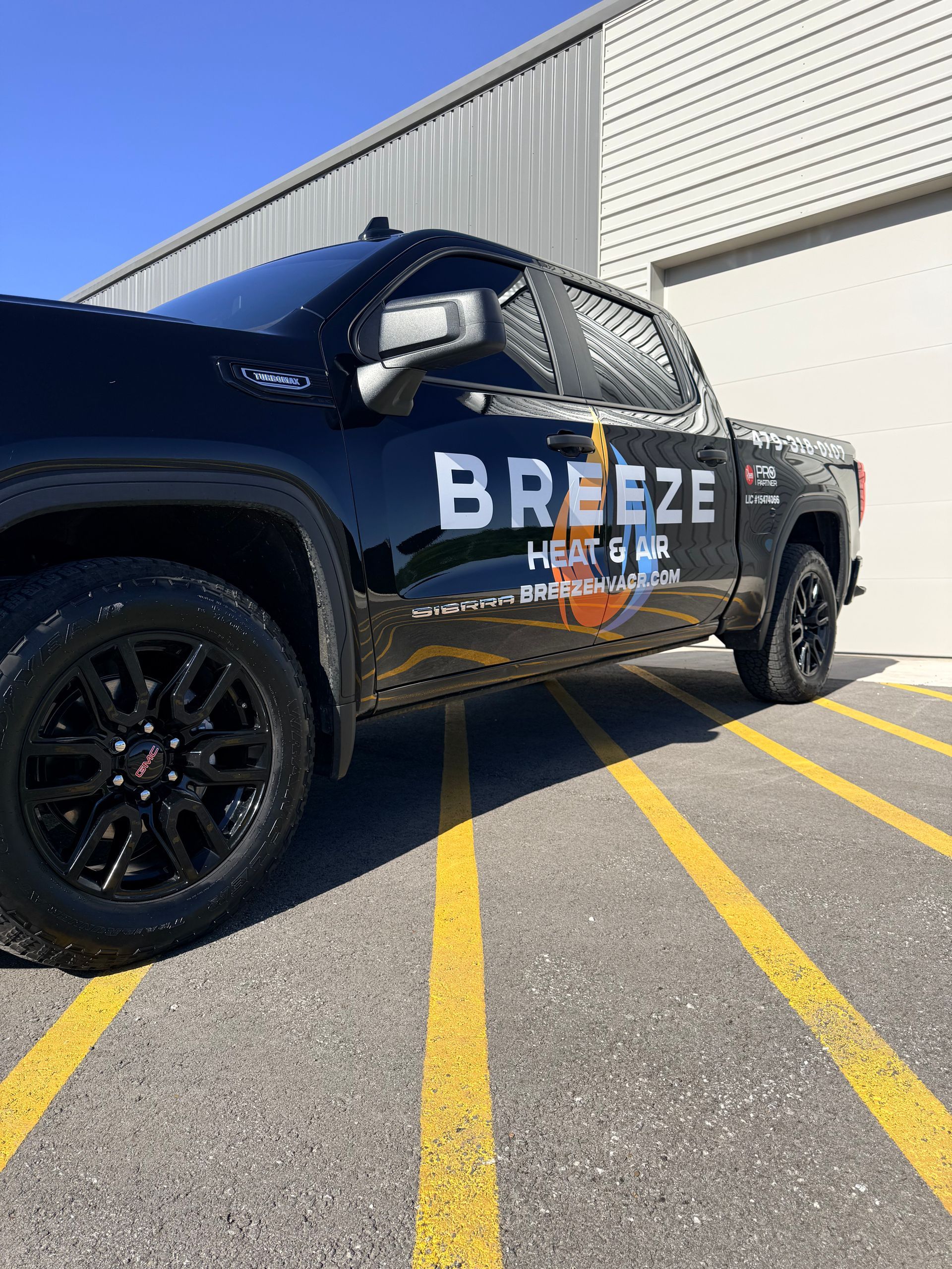 Black Breeze Heat truck parked in a lot beside a white building, viewed from the front side.