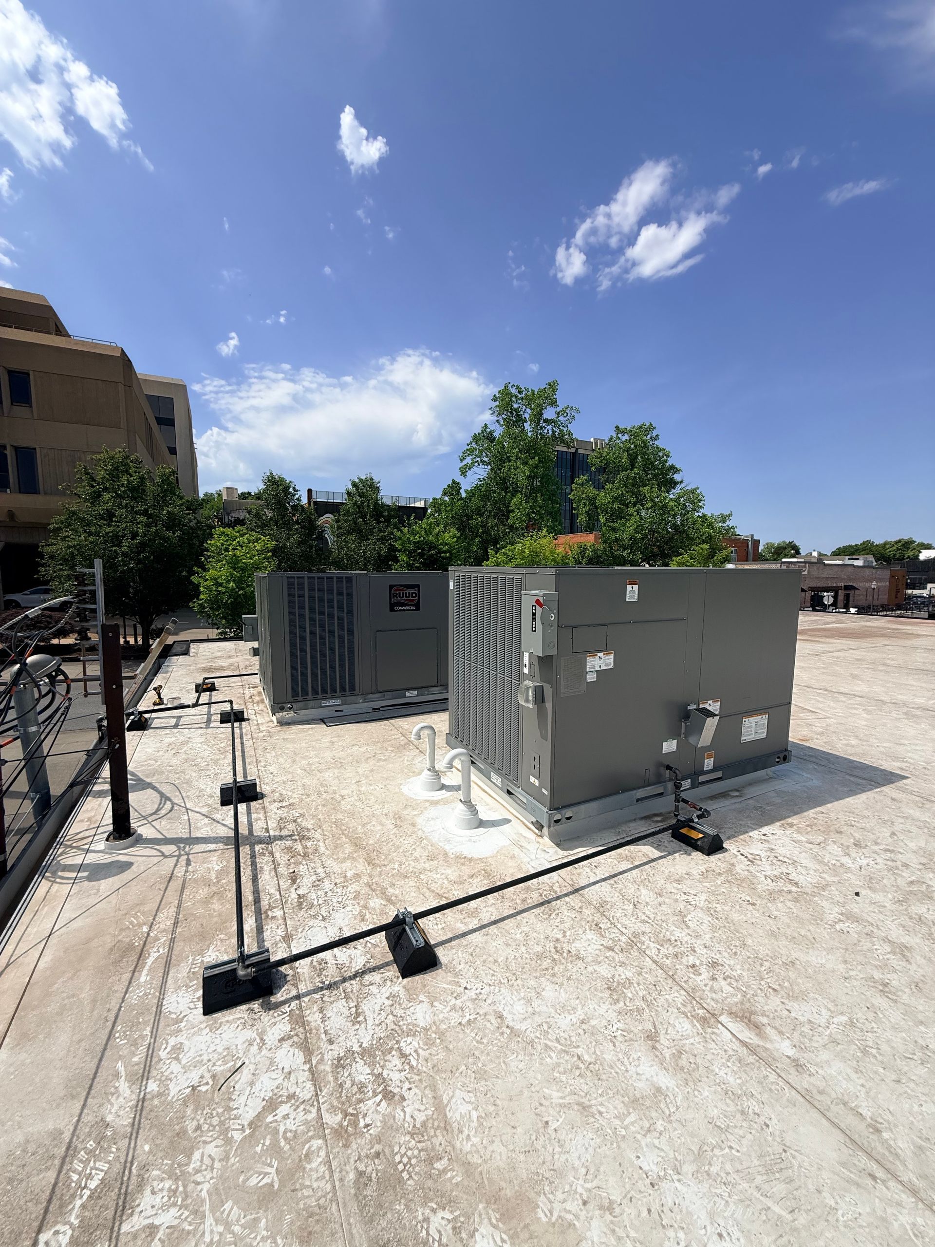 Outdoor rooftop with HVAC units, black sensors, and cables under a bright blue sky.