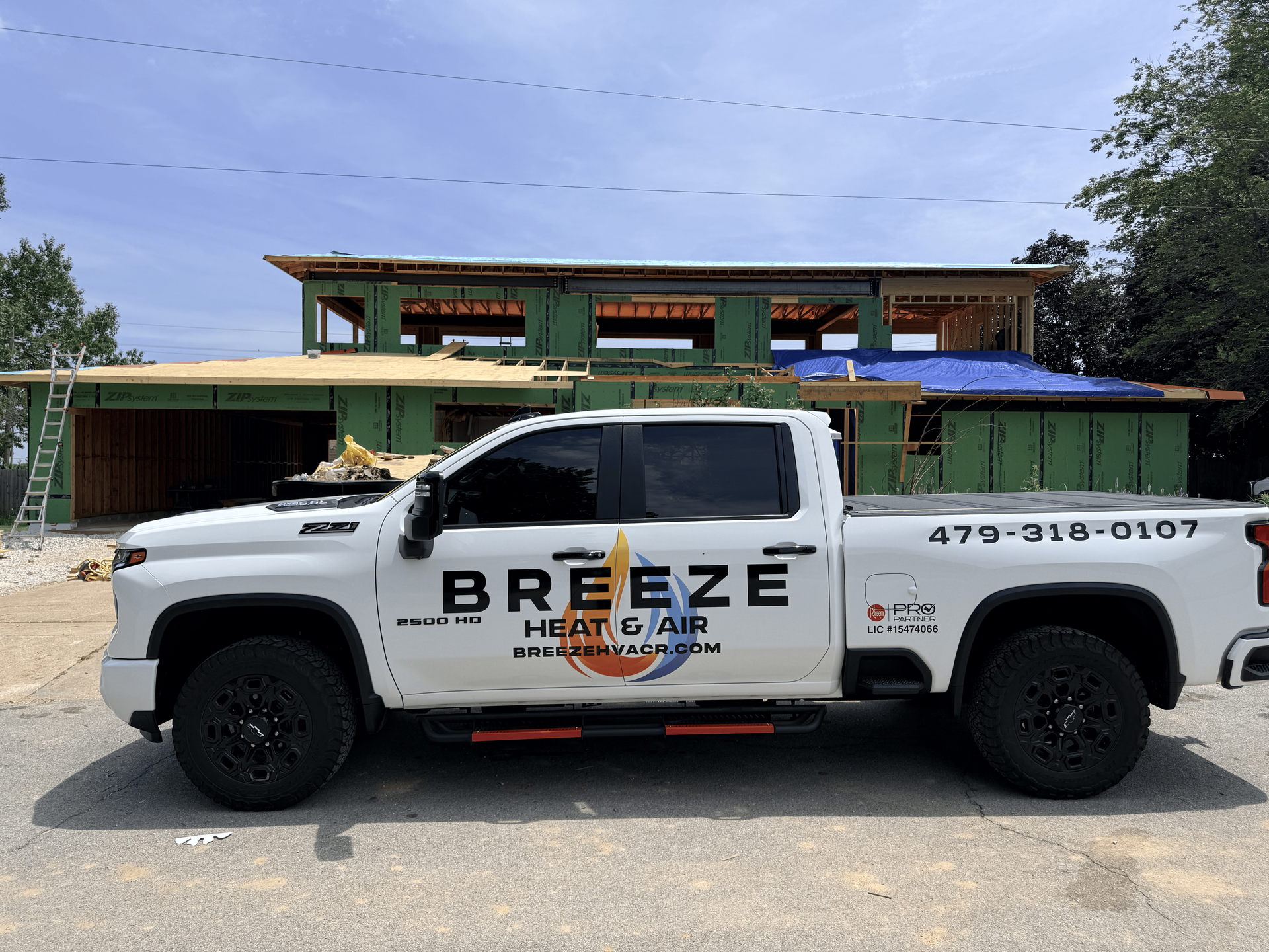 White BreezE HVAC service truck parked in front of a green building under a blue sky