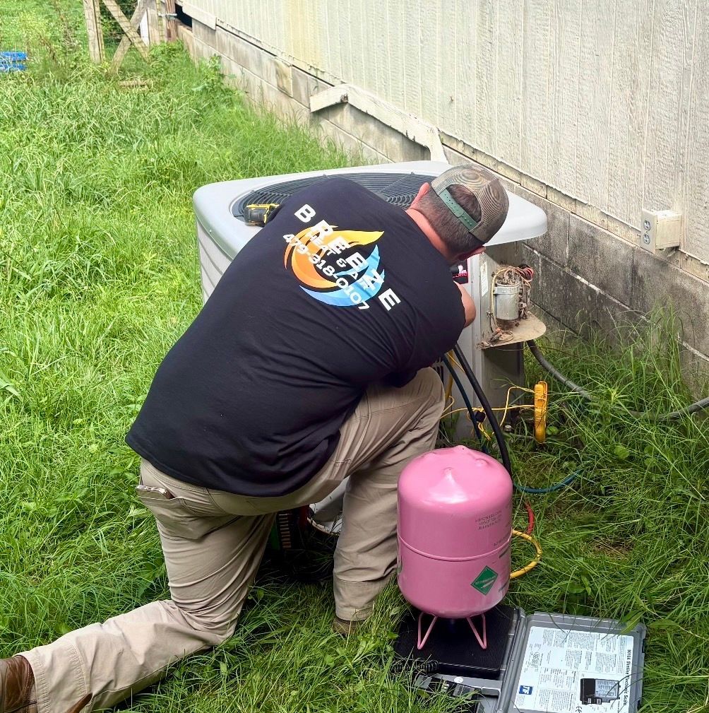 Person kneeling beside a house, working on outdoor propane equipment with pink tank and tools on grass