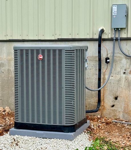 Outdoor HVAC unit against a beige building wall beside electrical boxes and conduit.