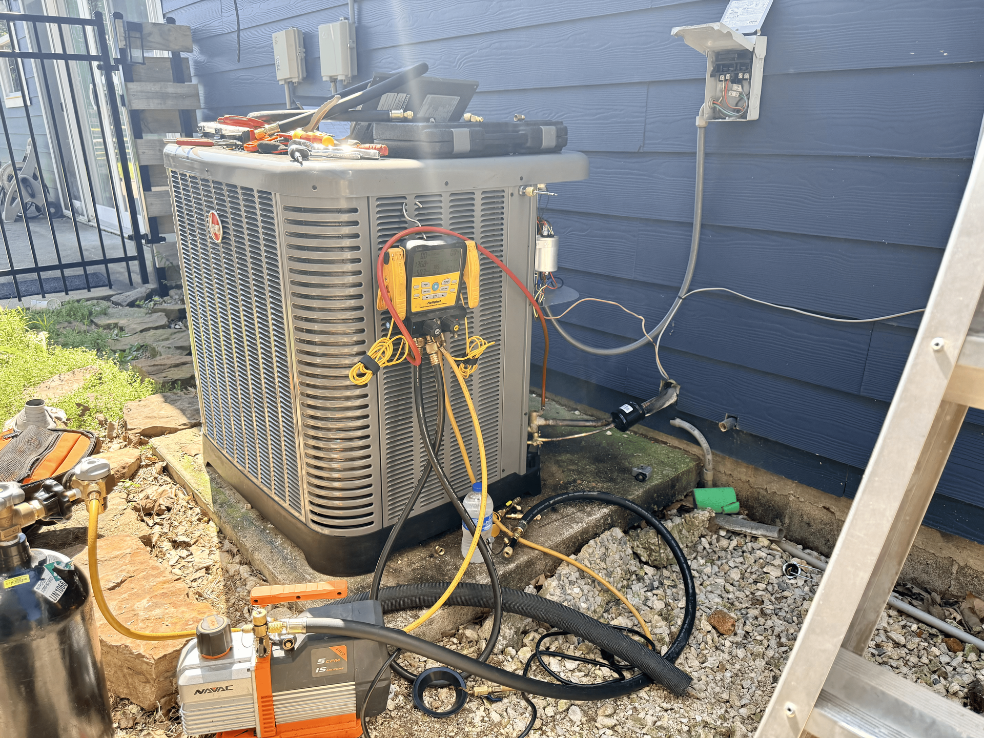 Outdoor HVAC unit with tools on gravel beside a blue house wall