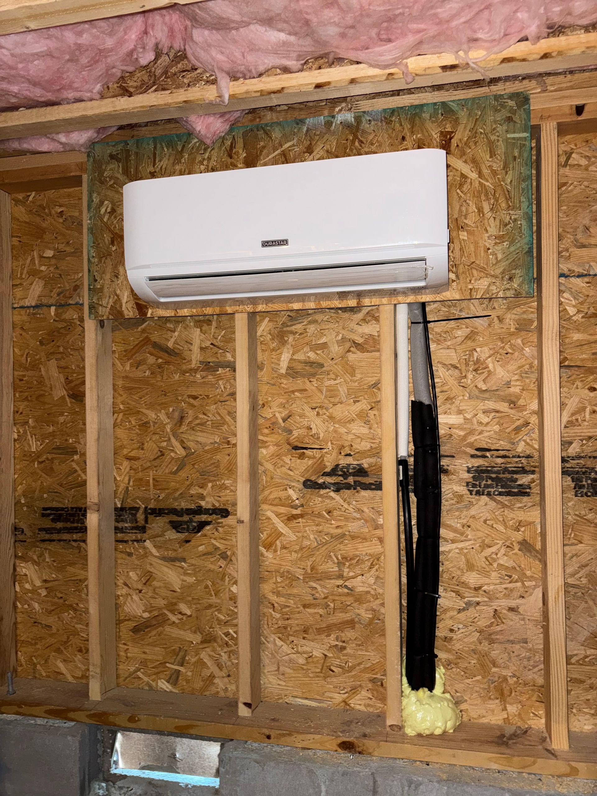 Wall-mounted white mini-split AC unit installed in an unfinished room with exposed studs and insulation.