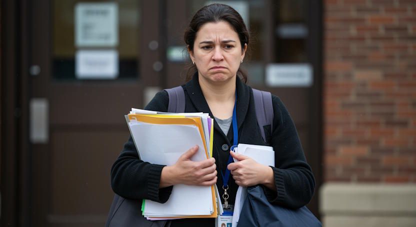 Teacher in Columbus leaving school at end of day, carrying paperwork spilling over and very tired