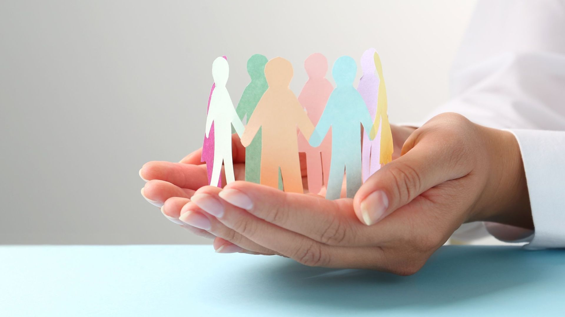 Different colour paper cut-outs of people being held in hands.