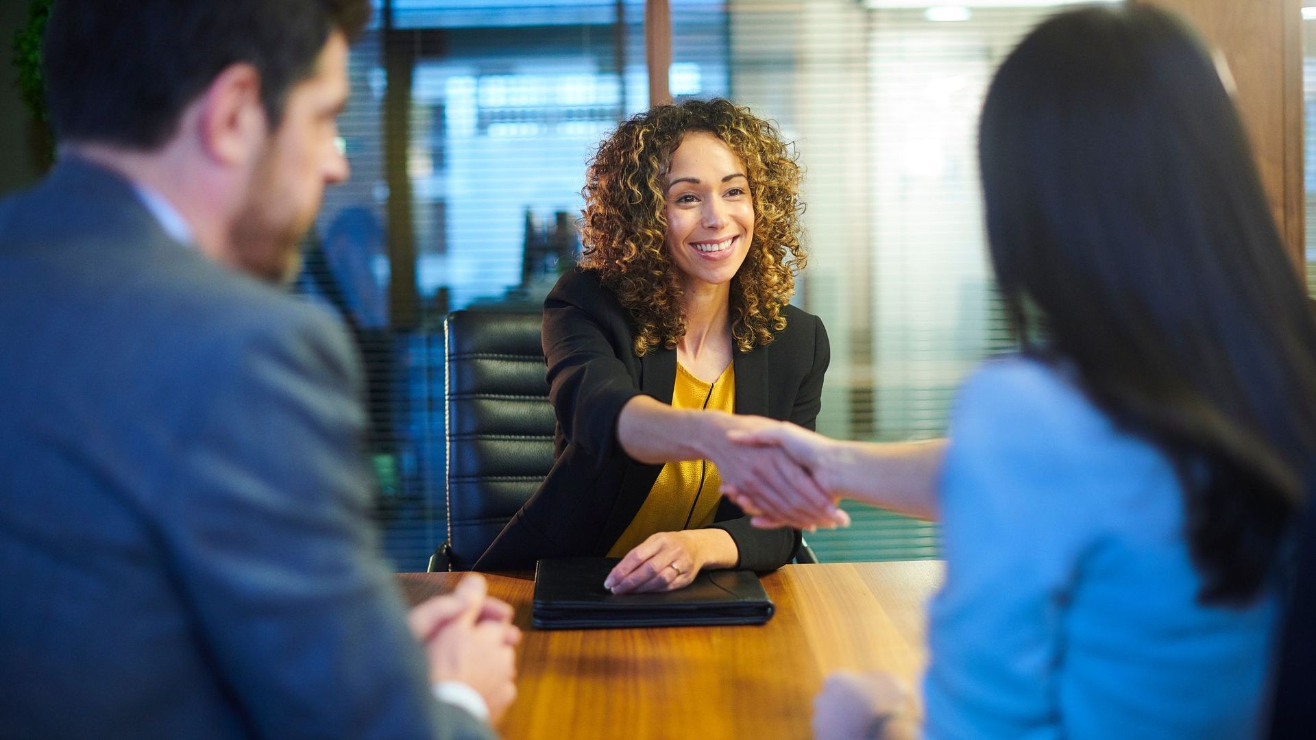 People in a work setting, shaking hands across a table. 