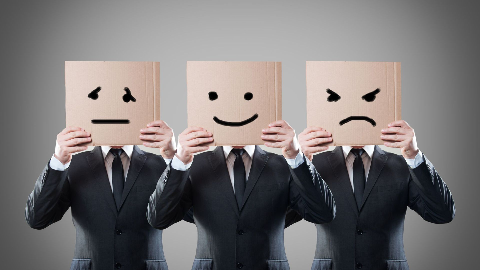 People in suits holding boxes over their faces with faces painted on them. 
