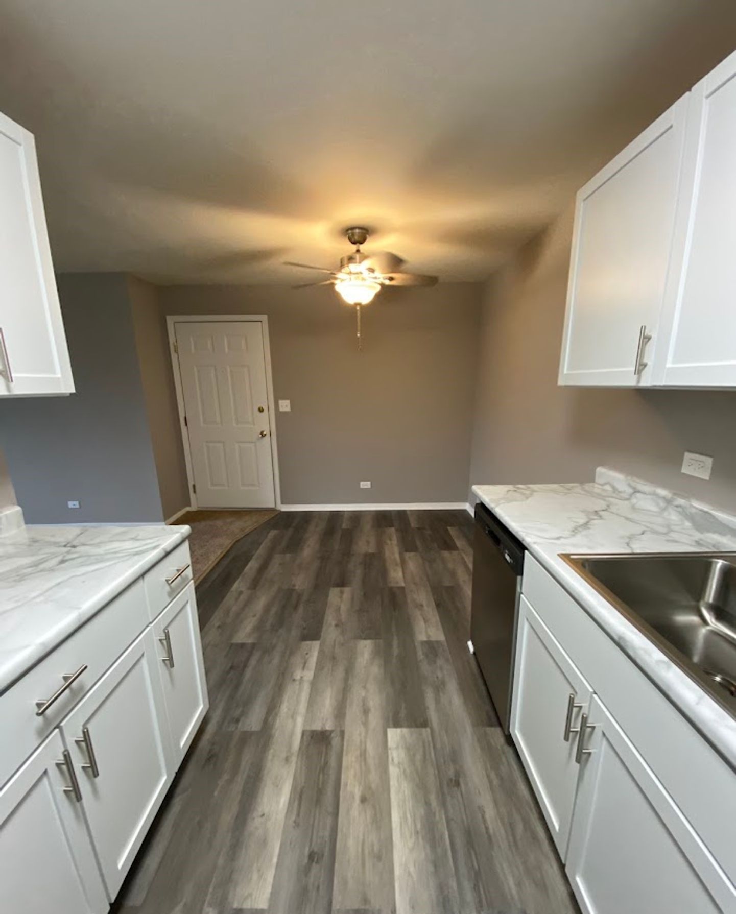 A kitchen with white cabinets , a sink , and a ceiling fan.