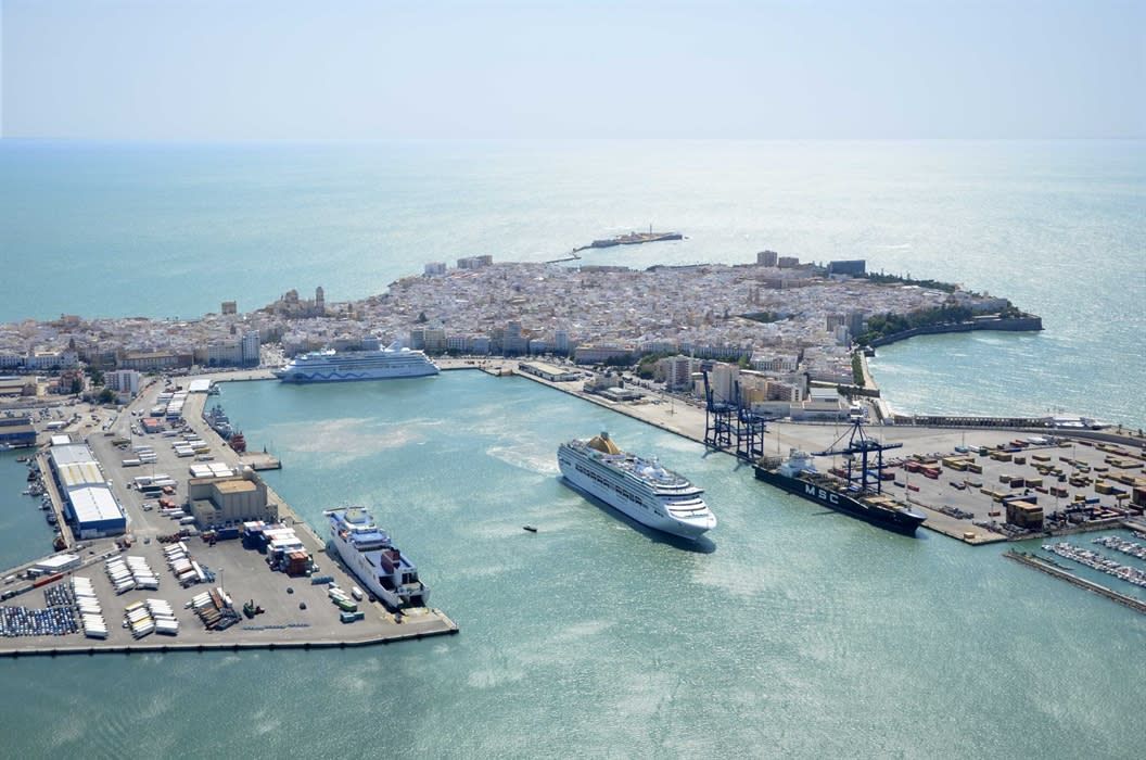 Majestic luxury cruise ship docked at a modern port terminal, with the historic city skyline visible in the background under a bright morning sky.