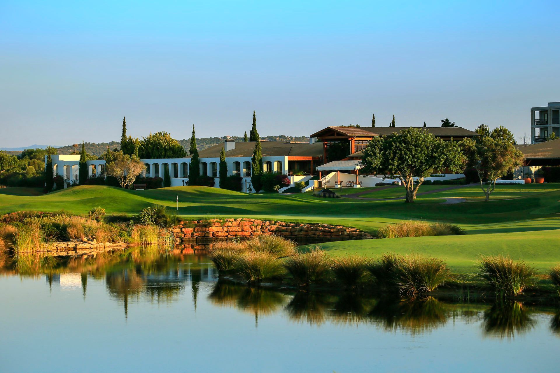 Sophisticated sunset event on a golf course terrace, overlooking the 18th hole with rolling hills and a modern clubhouse in the background.
