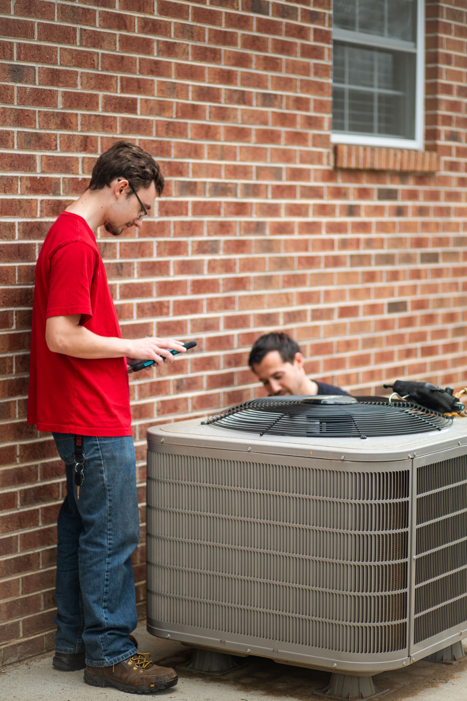 A white air conditioner is sitting on the side of a house next to a window.