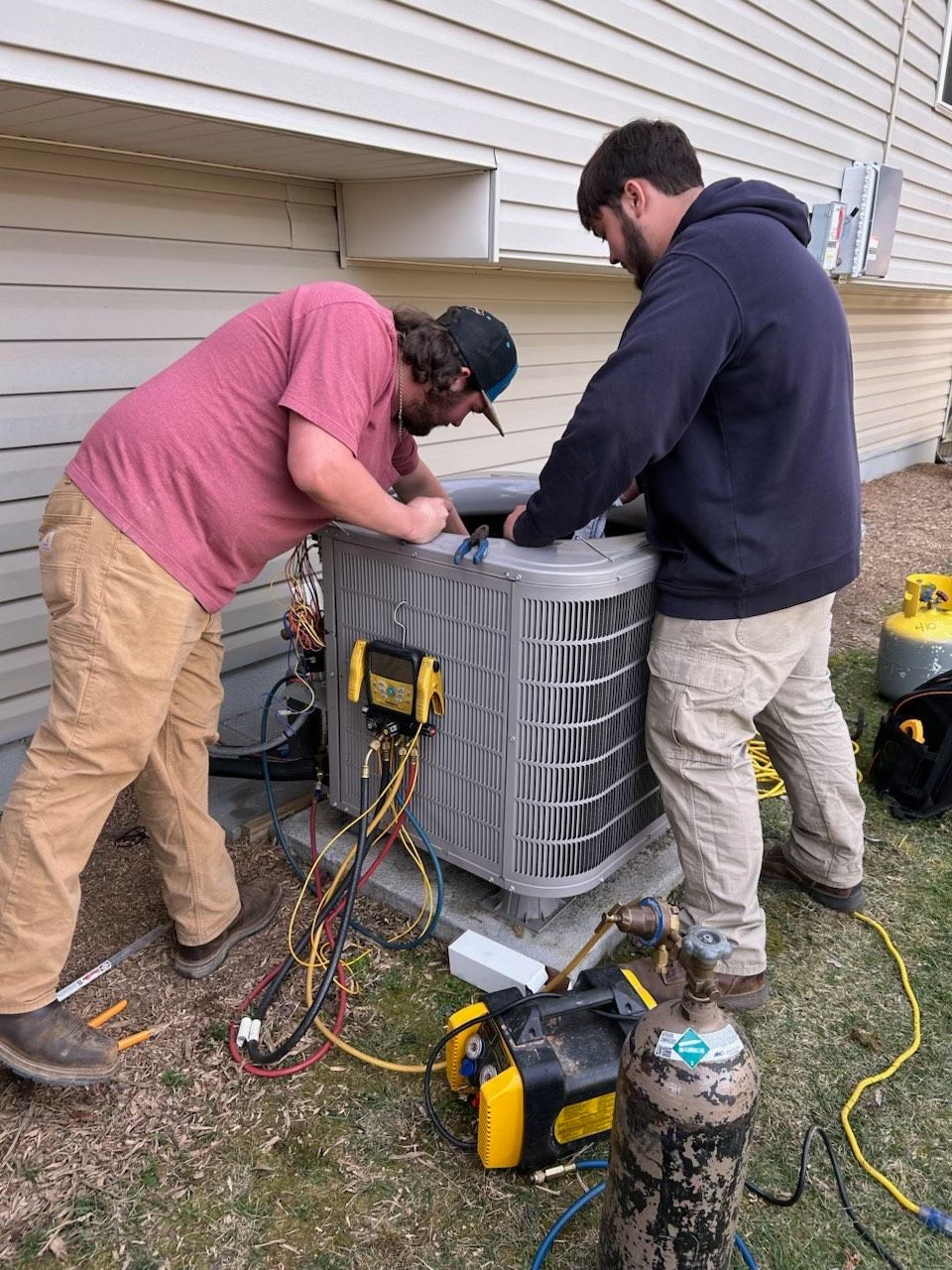 Two men are working on an air conditioner outside of a house.