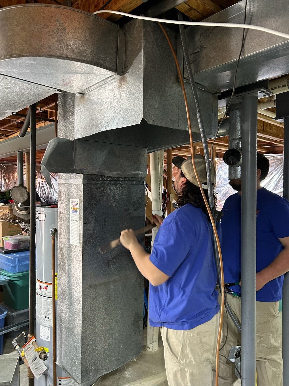 A man is working on a ventilation system in a basement.