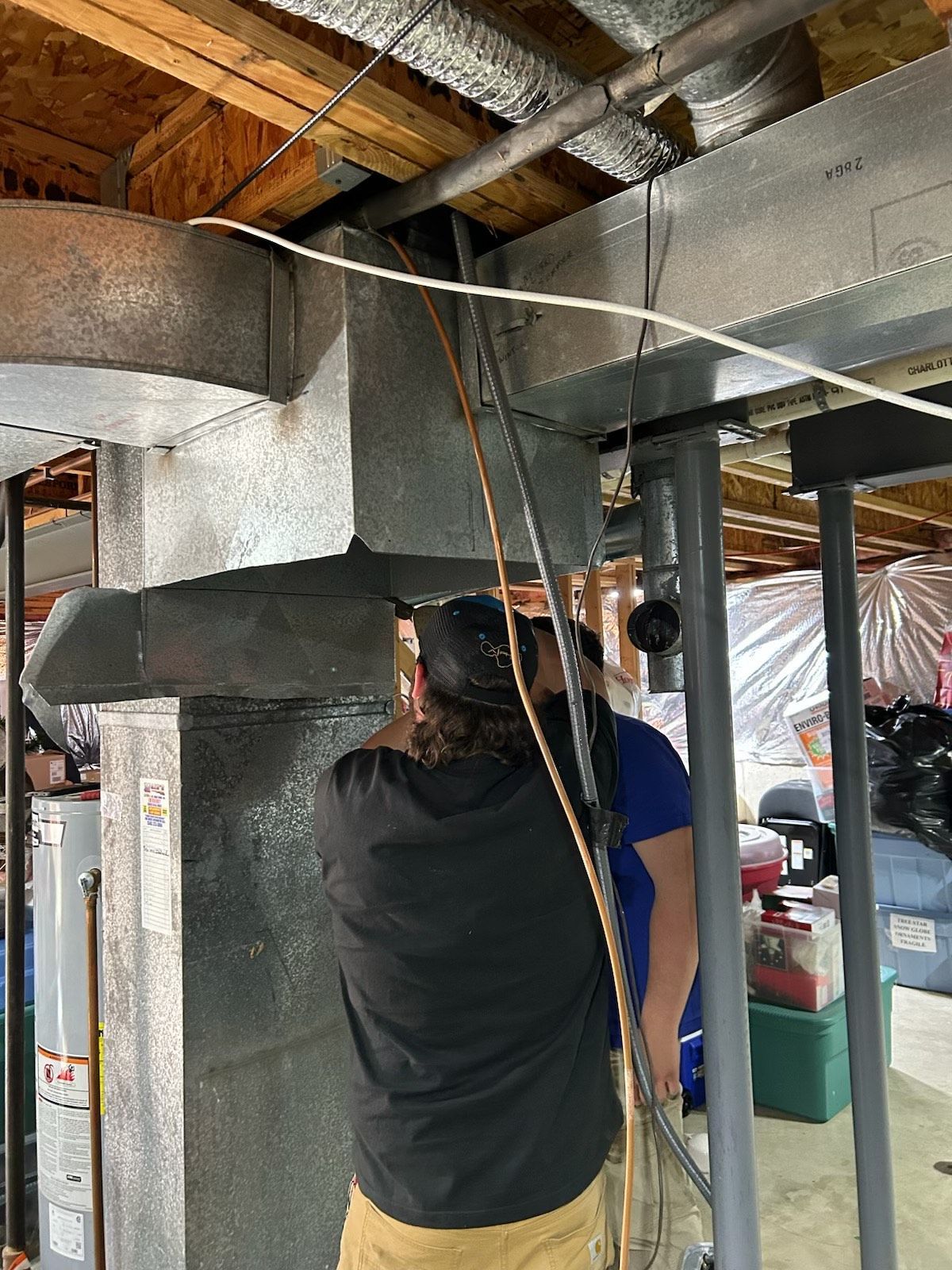 A man is working on a ventilation system in a basement.