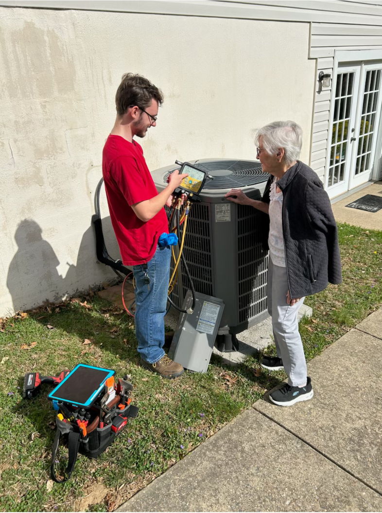 A man and a woman are standing next to an air conditioner.
