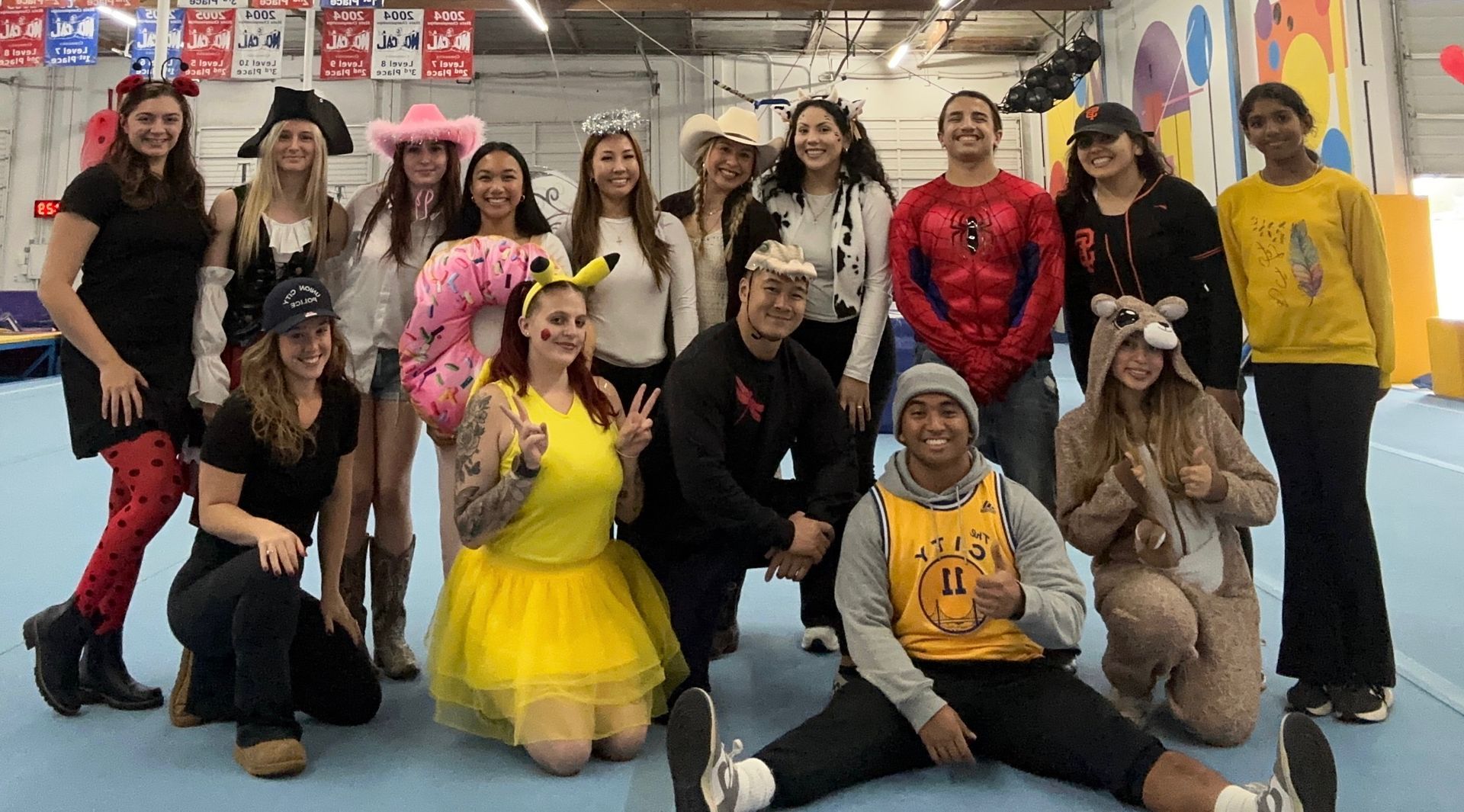 Group of people in costumes posing indoors near gym equipment.