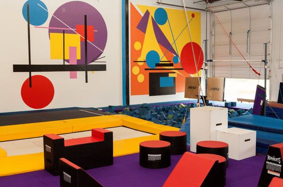 Indoor parkour gym with colorful abstract murals, mats, and obstacles.