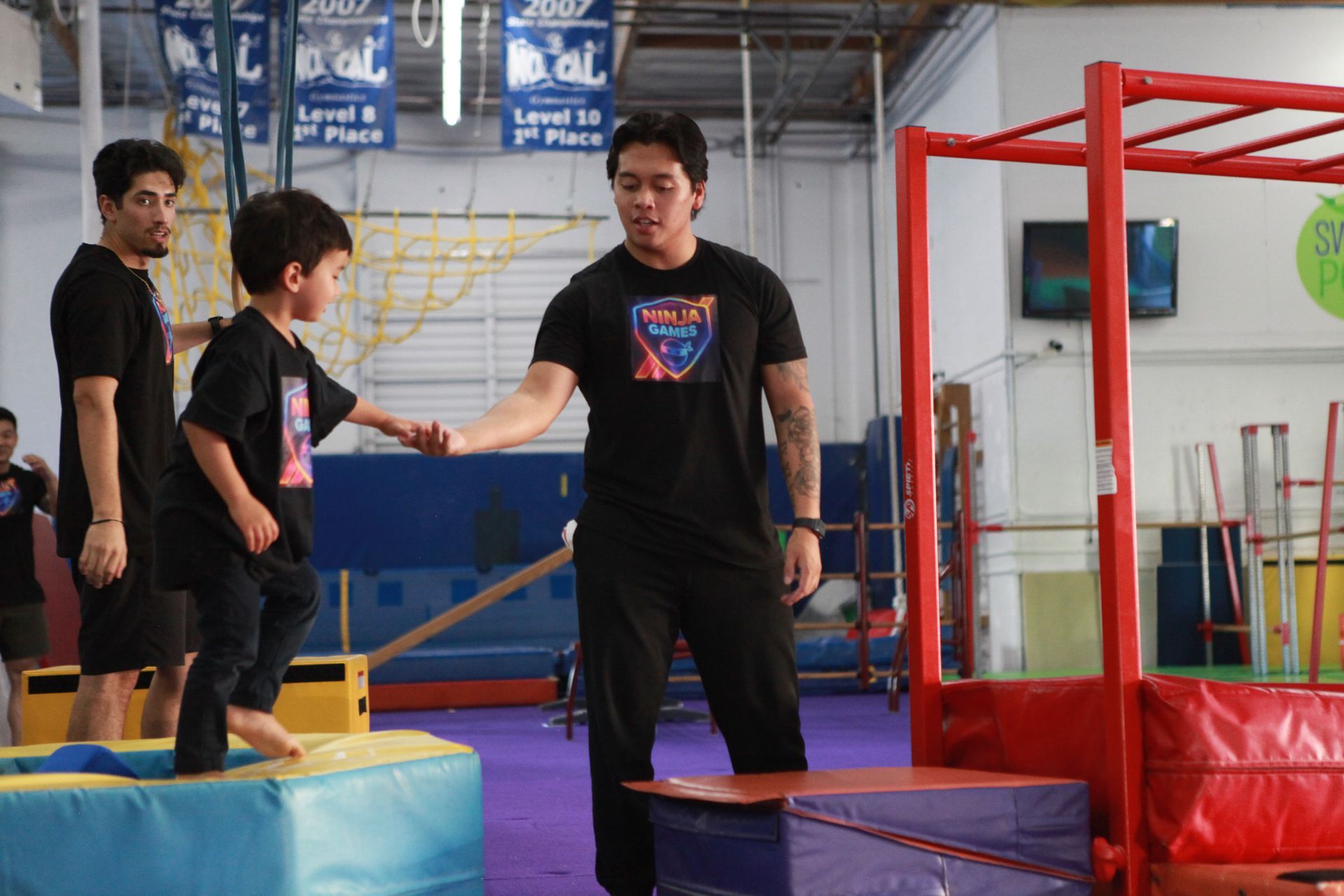 A boy and two men in an obstacle course gym. The boy and one man are high-fiving.